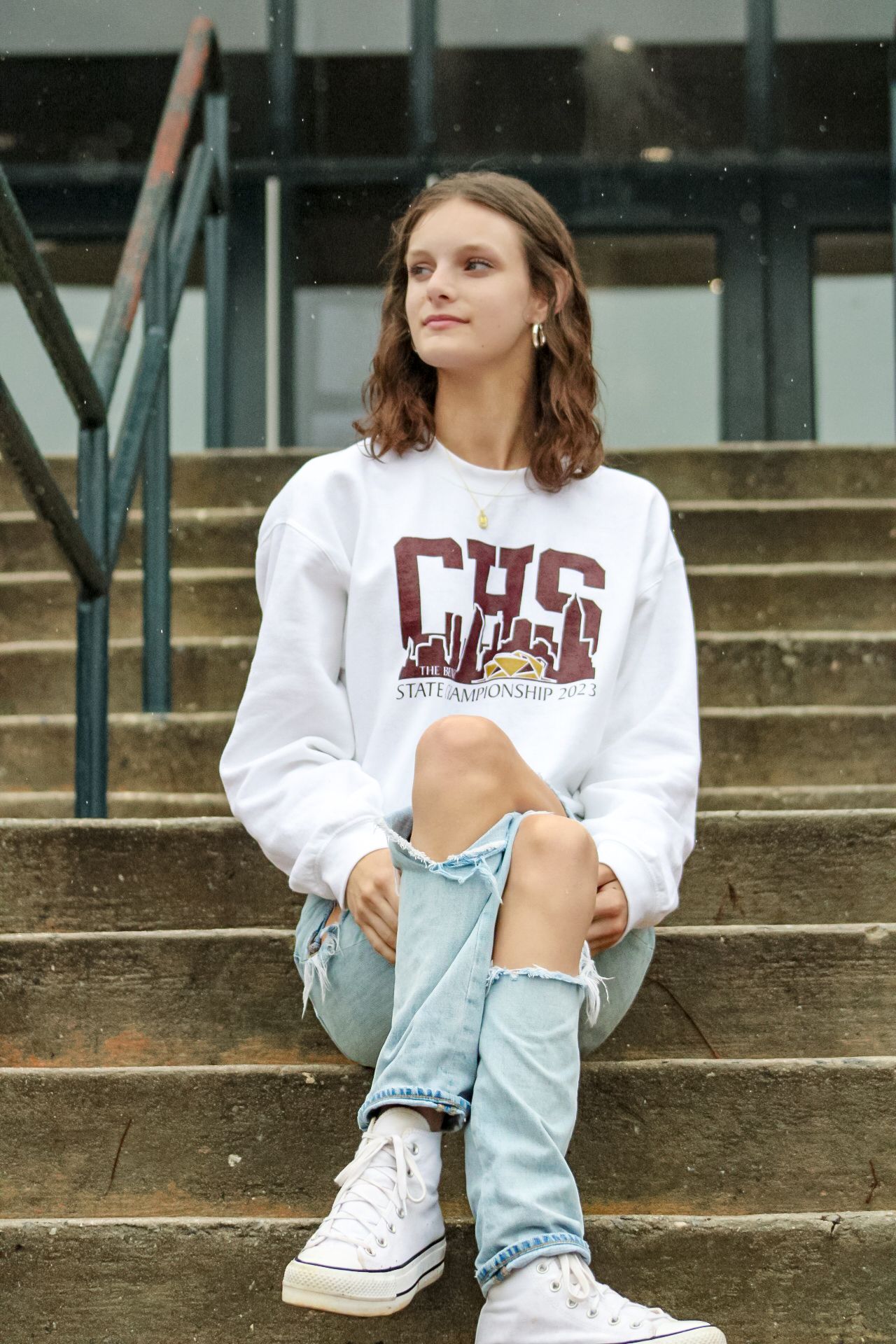 Teen girl sitting on stone steps in white CHS State Championship sweatshirt and distressed jeans.