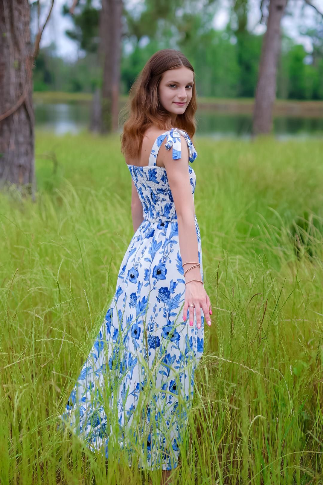 A person in a blue and white floral dress twirls in a tall grass field on a sunny summer day.