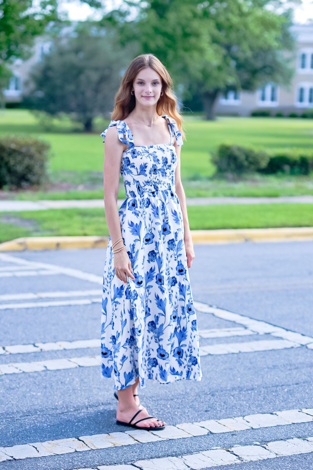 Young woman wearing white and blue floral maxi dress standing on suburban street.