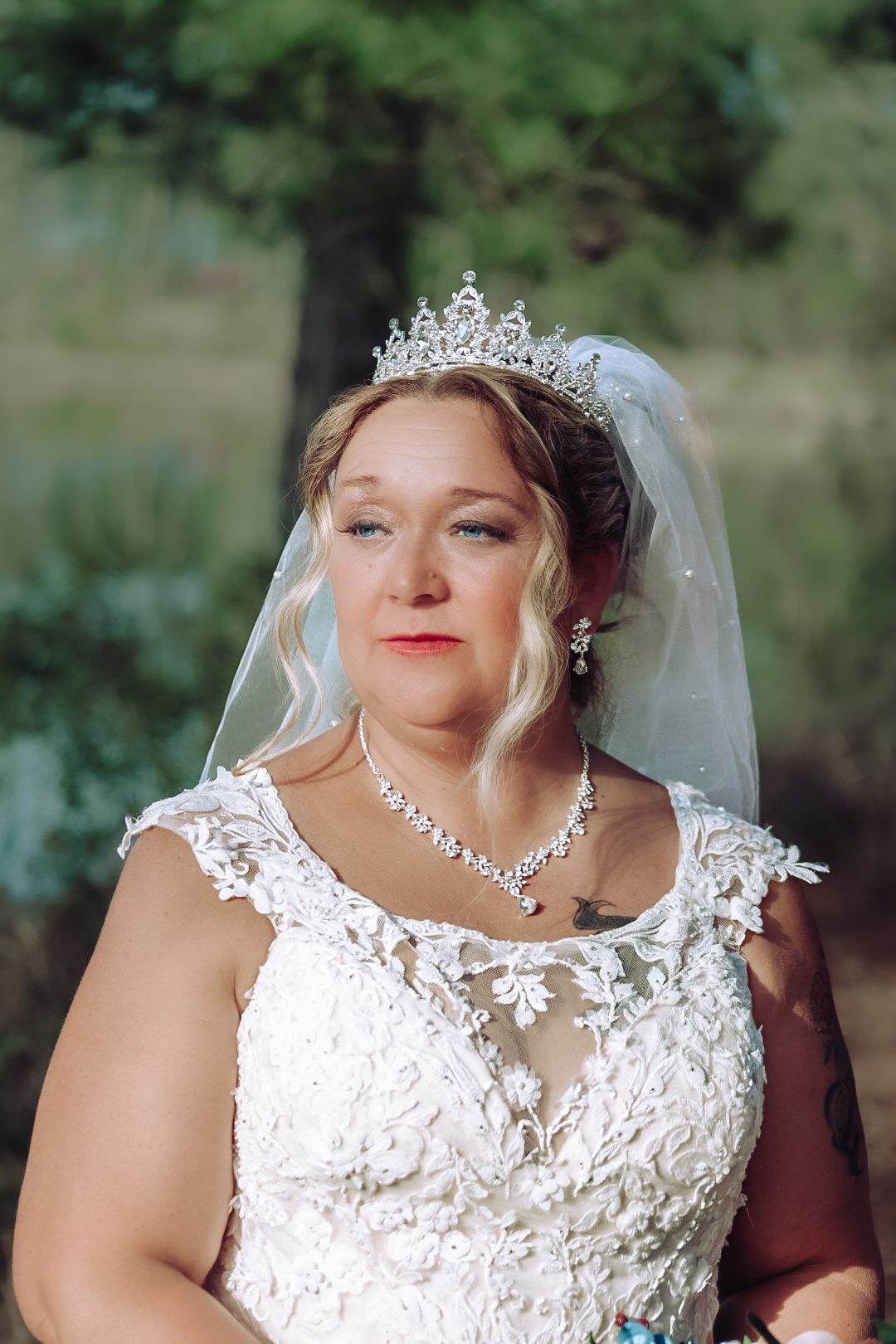 A bride wearing a white lace wedding dress with crystal accessories including a tiara, necklace and veil.