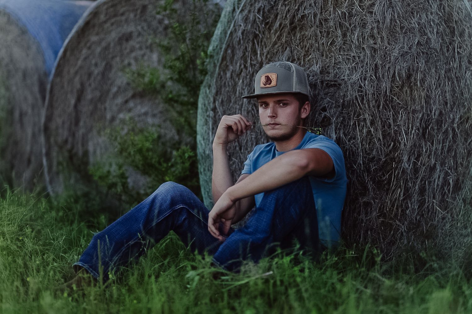 A person in casual clothing sits against a tree trunk in a natural outdoor setting with green foliage in the background.