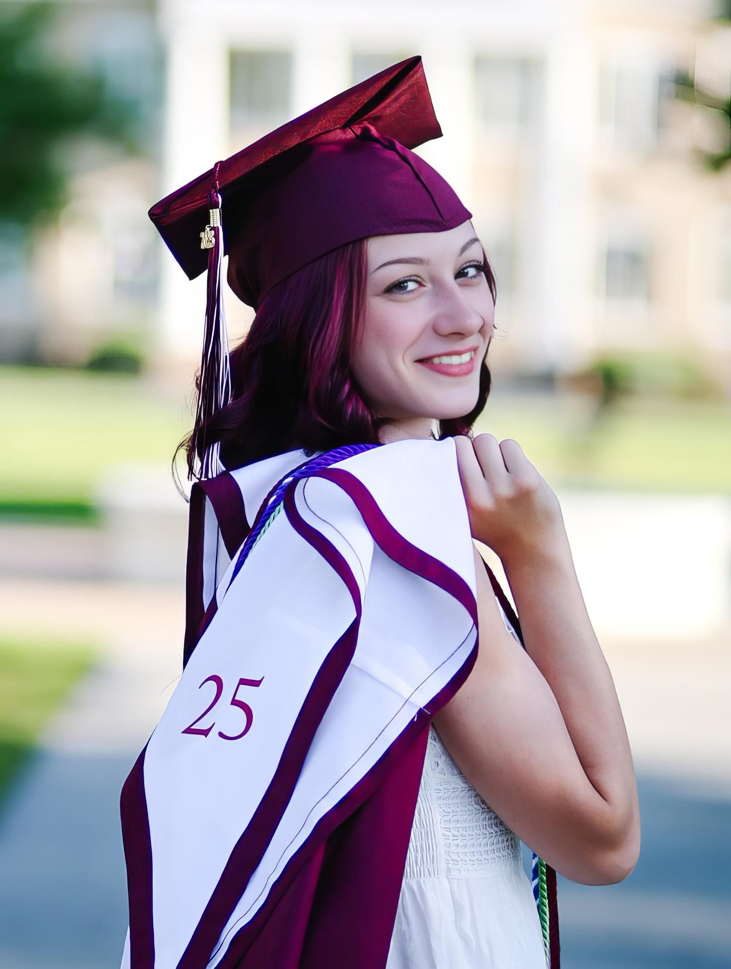 Graduate in maroon cap and gown smiles during outdoor graduation photo session at university.