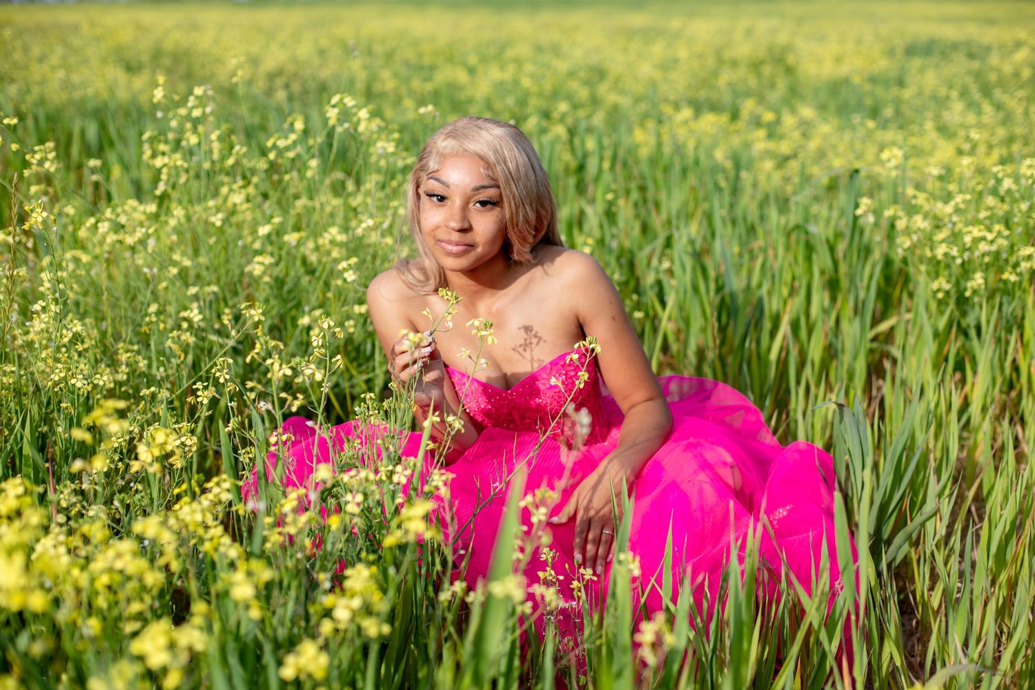 A person in a vibrant pink dress poses gracefully among blooming yellow wildflowers in a summer meadow.