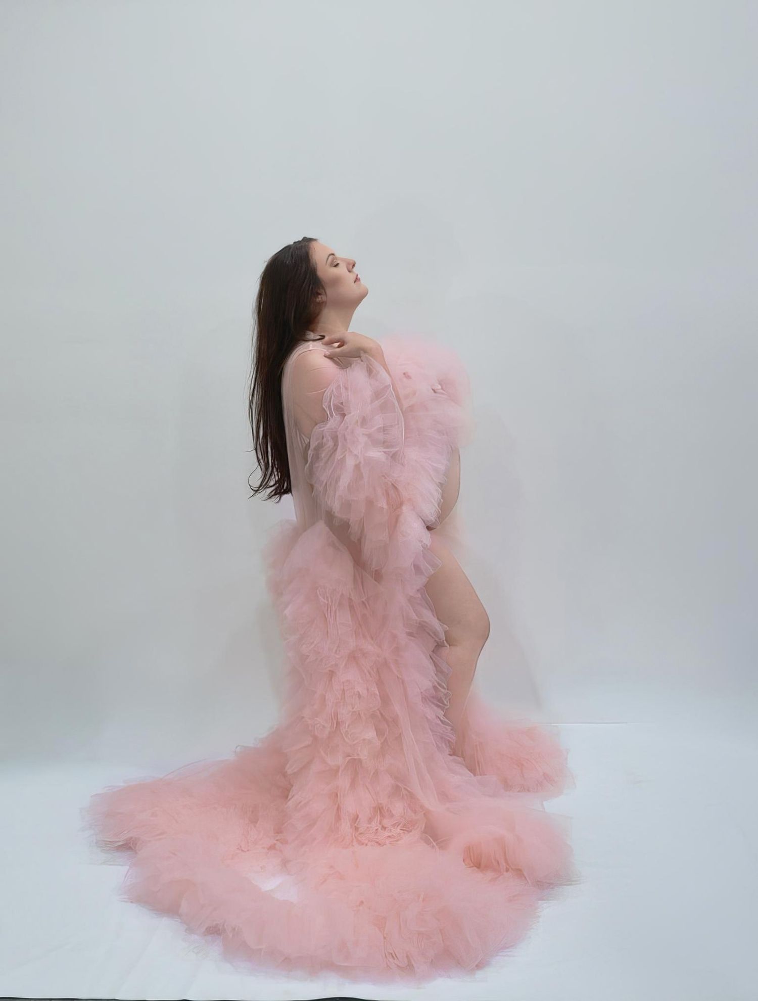Woman posing in a flowing pink tulle robe with ruffled trim against a white background.