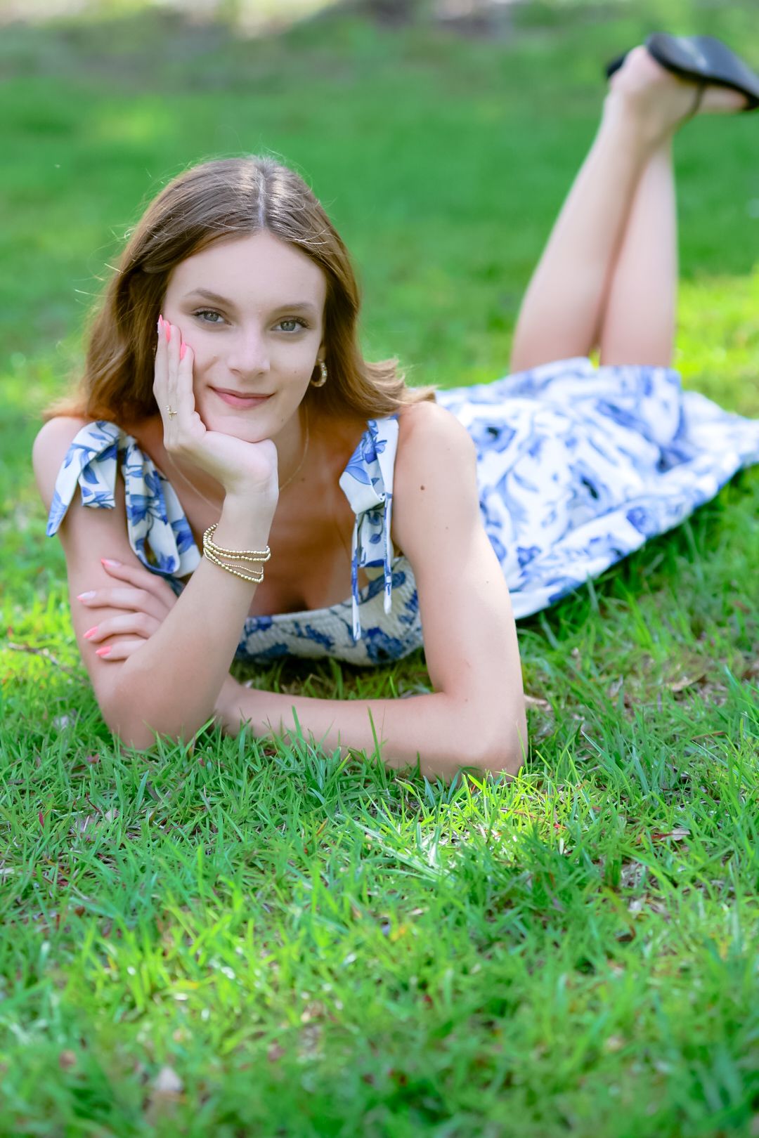 Smiling young woman in blue floral dress lying on green grass in park.
