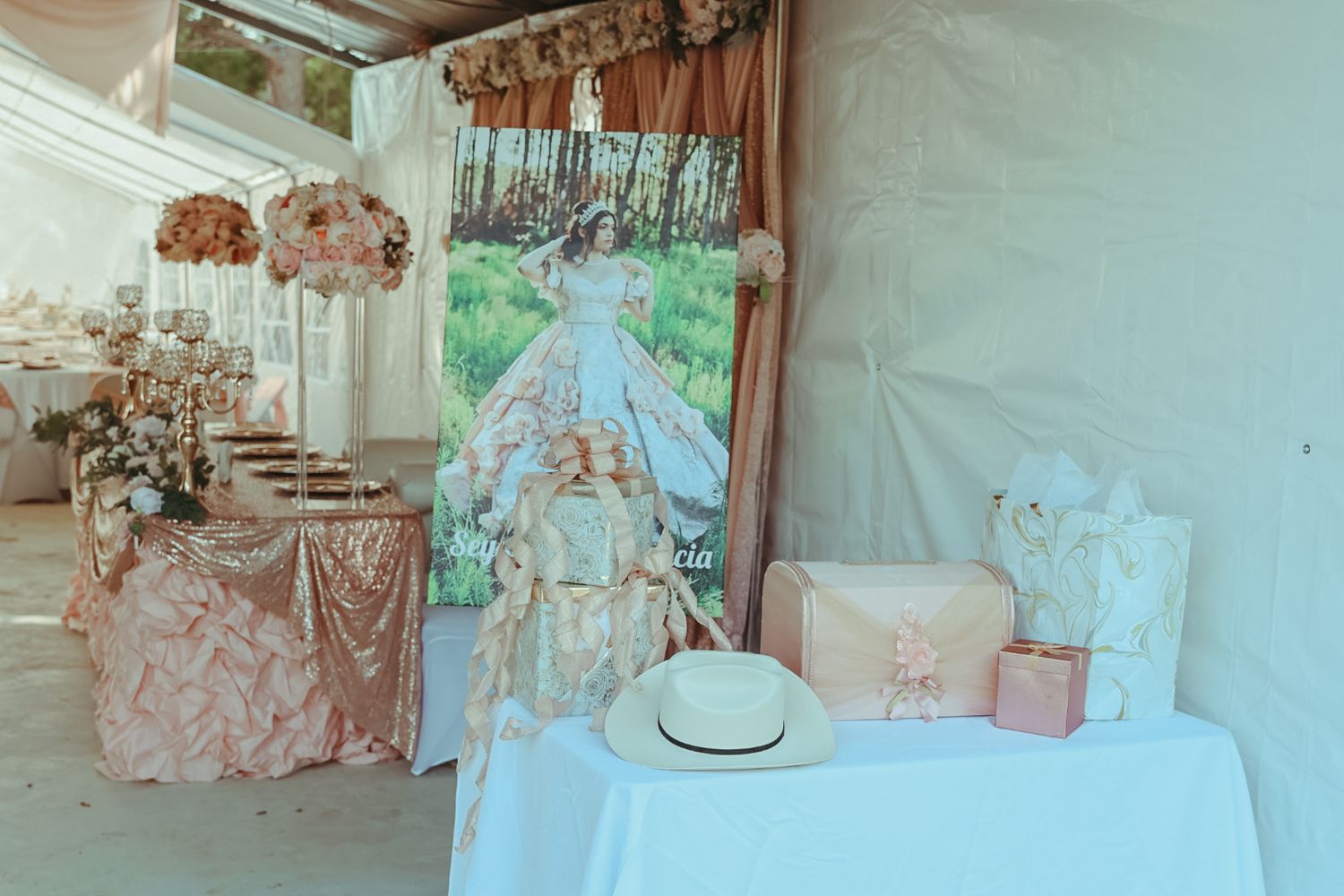 Elegant quinceañera decoration setup with blush pink tablecloths, floral arrangements, and a portrait backdrop display.