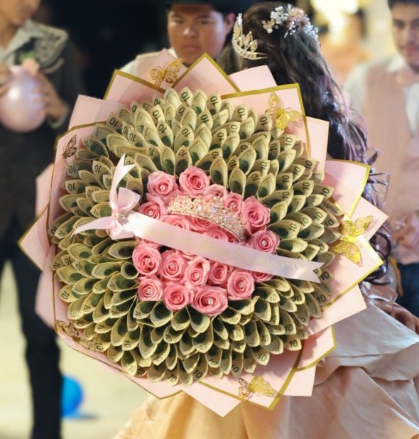 Elegant bouquet of pink roses surrounded by fanned green leaves with gold accents, held at a formal event.