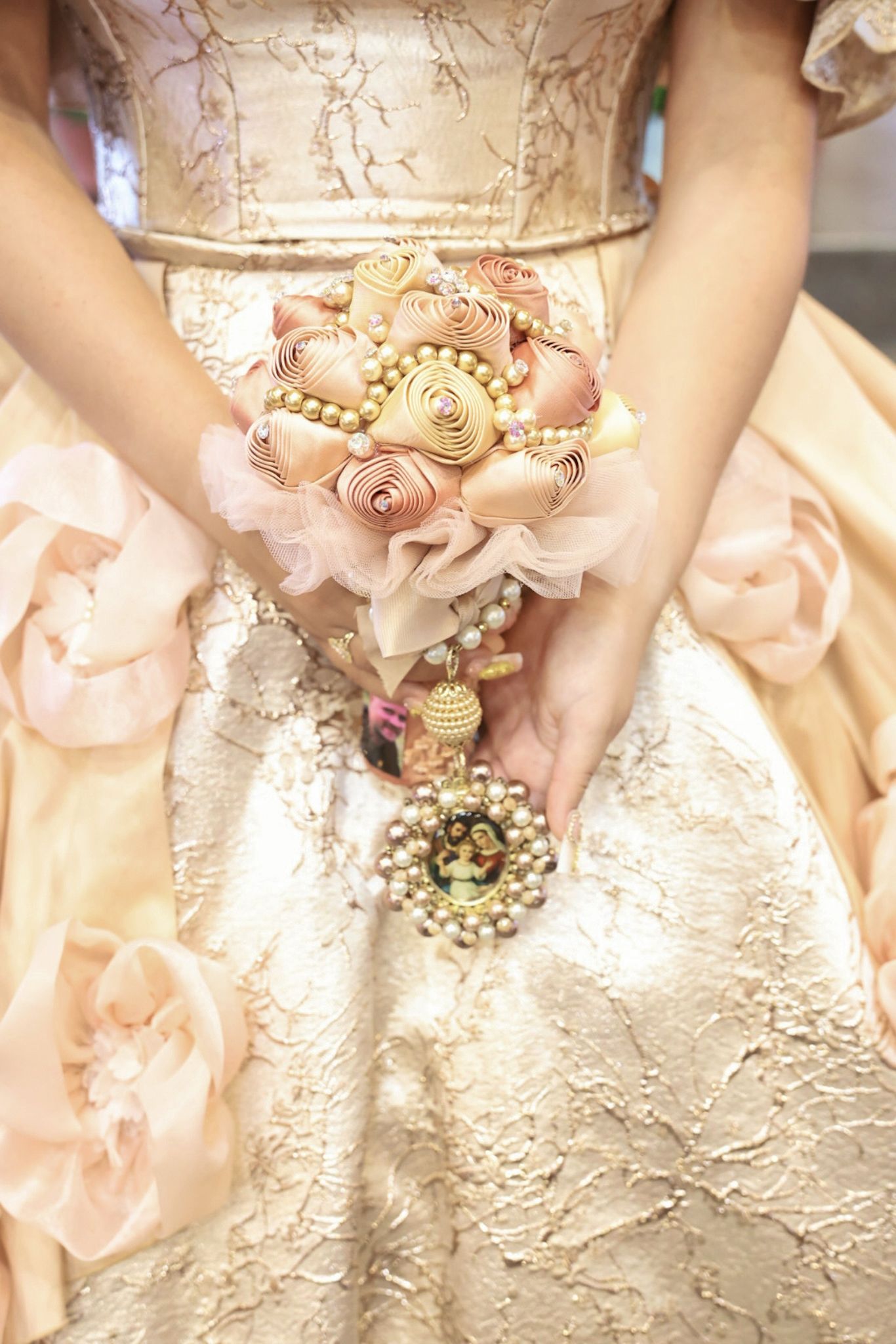 Bride in gold gown holding ornate brooch bouquet with pearl roses and jeweled accents at a wedding ceremony.
