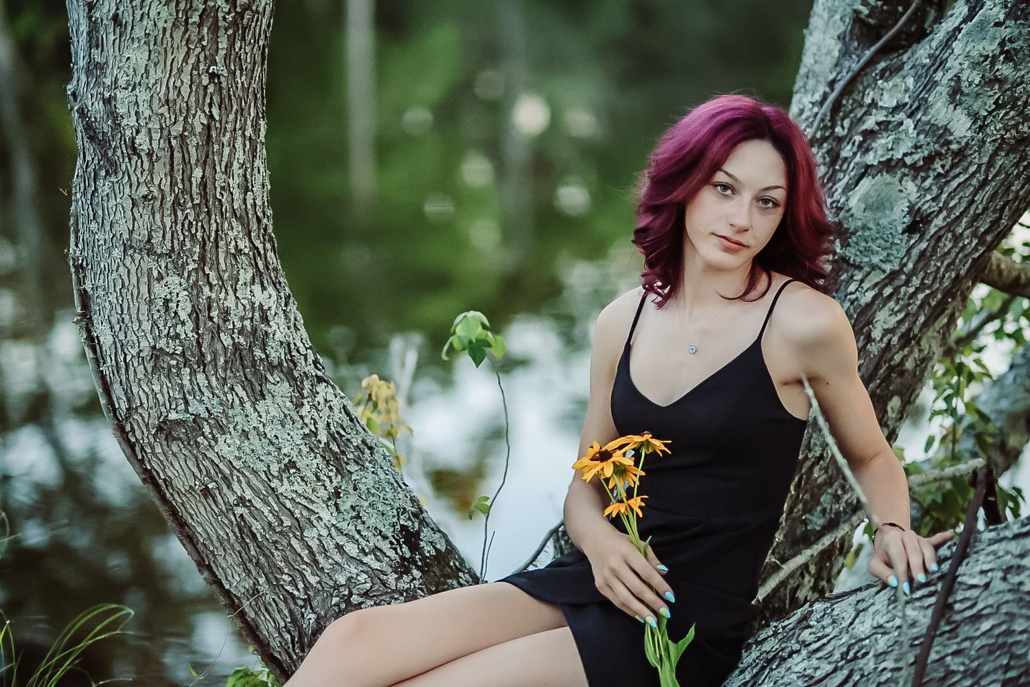 A figure in a black dress poses among tree branches with vibrant purple hair against a natural outdoor backdrop.