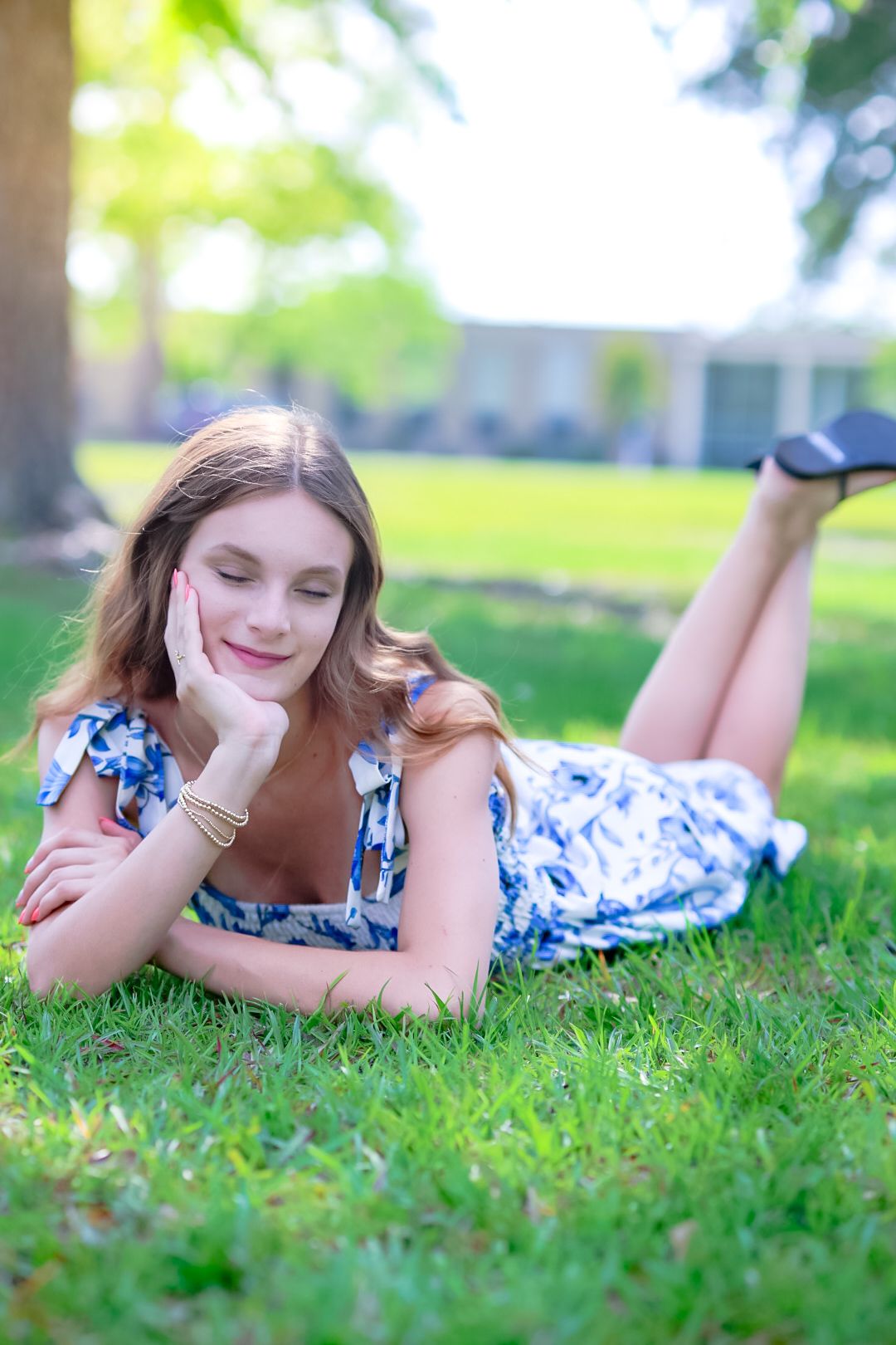 Young woman in blue floral dress lying on green grass in sunny park.