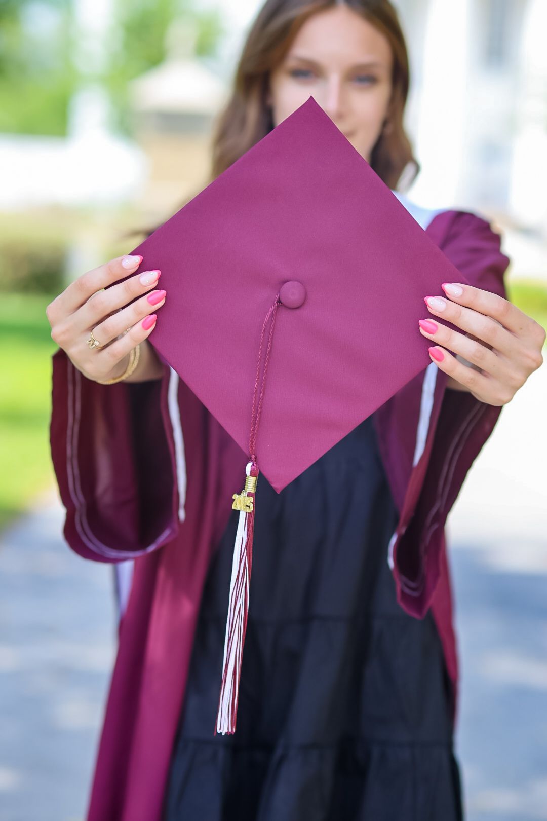 A burgundy graduation cap and gown with a pink mortarboard held up to display the tassel.