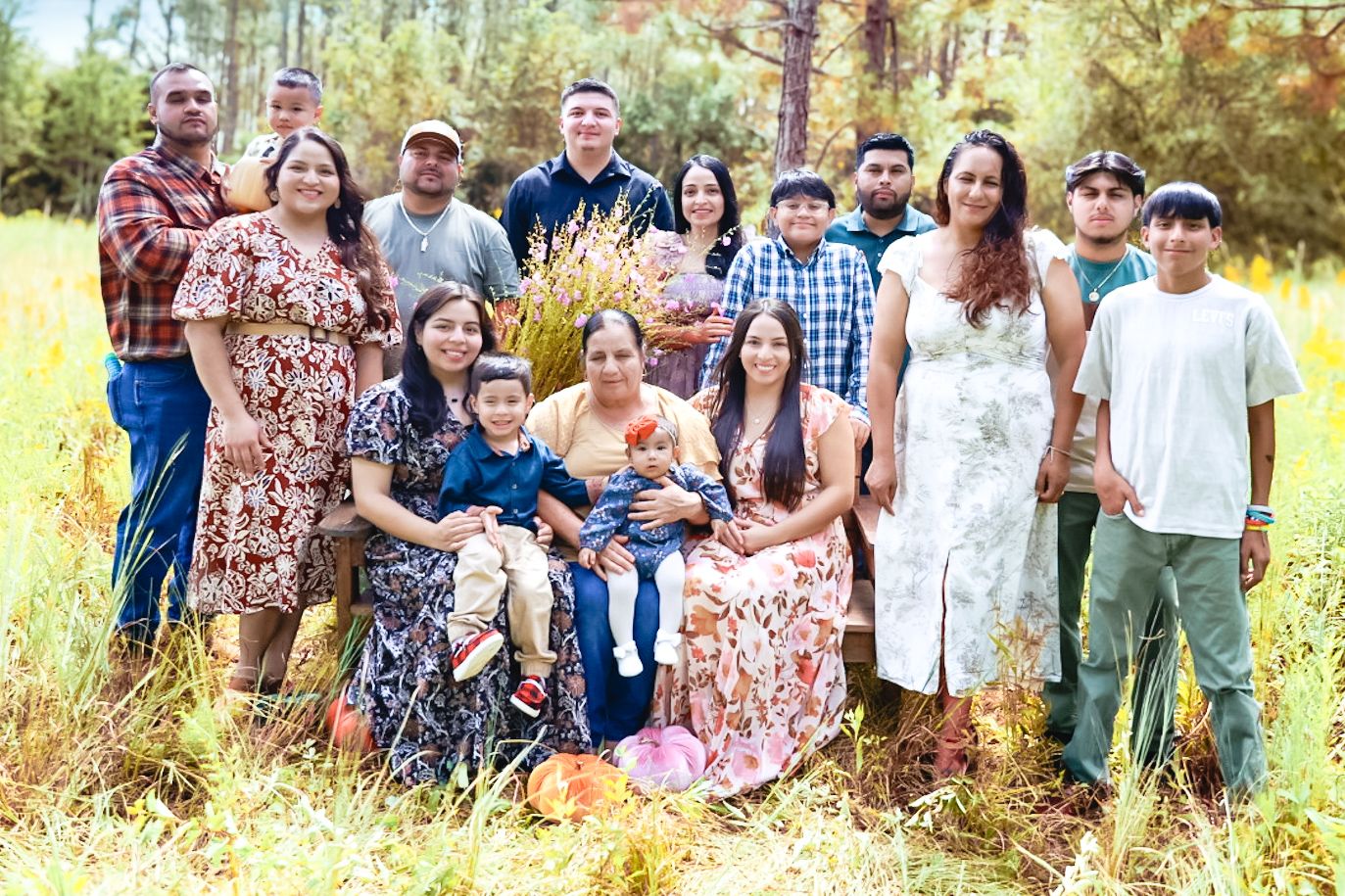 Large group enjoying a casual outdoor gathering in a wooded setting with sunlight filtering through trees.