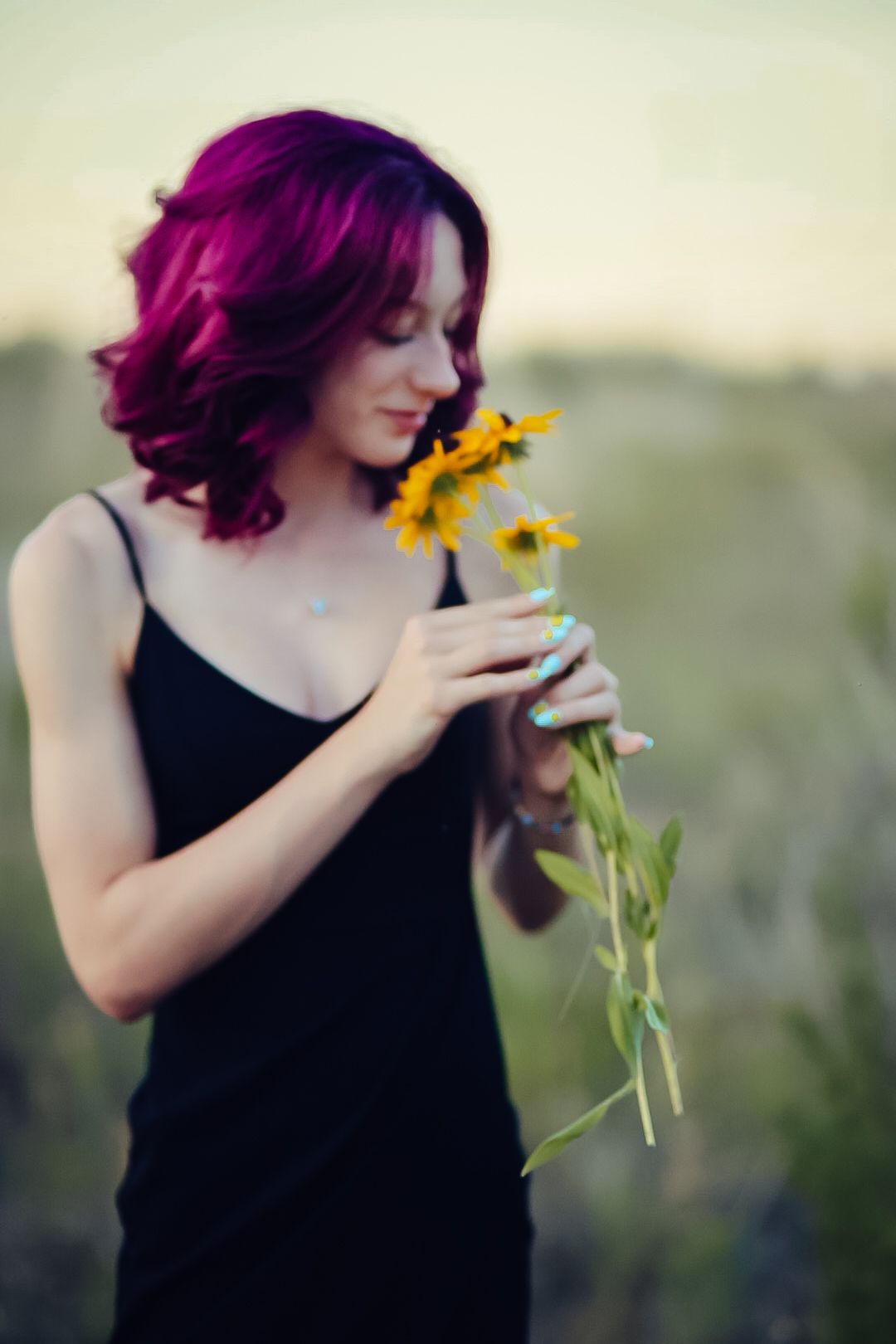 A figure in a black top smells bright yellow sunflowers against a soft blurred background.