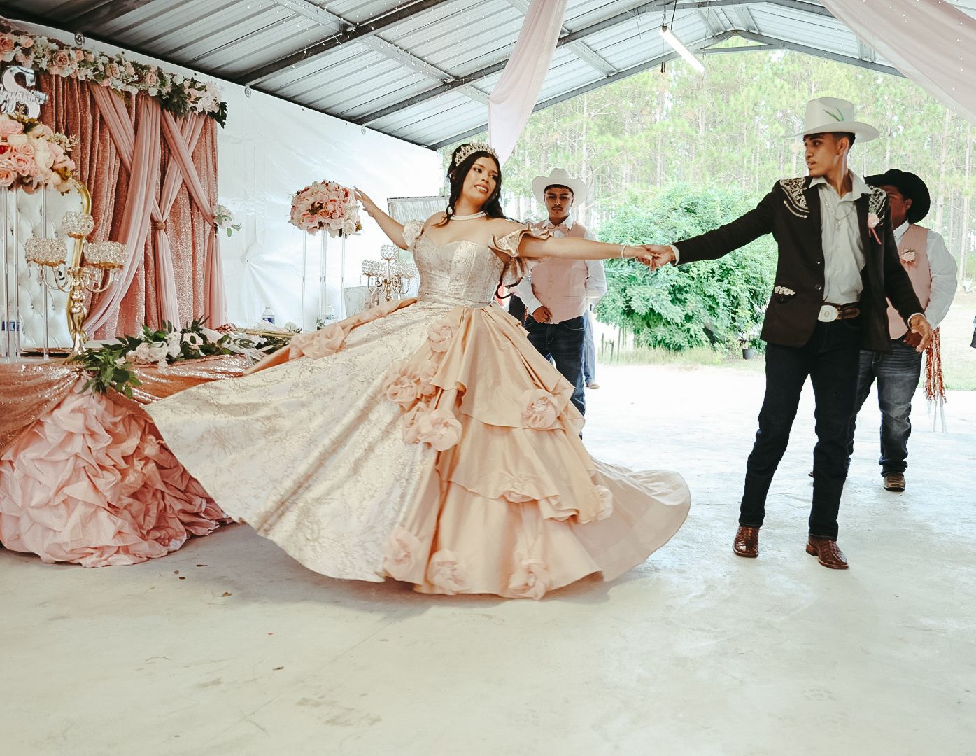 Young woman in a elegant pink quinceañera ball gown dancing with two men in a decorated event venue.