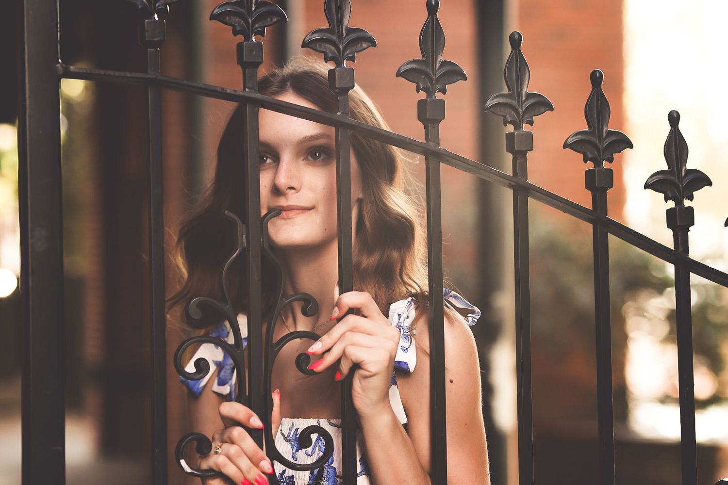 Young woman in colorful dress looking through ornate black iron gate.