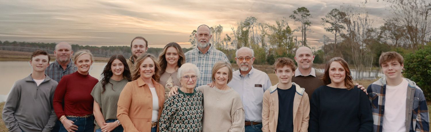 Large family gathering outdoors with scenic landscape and sunset sky in background.