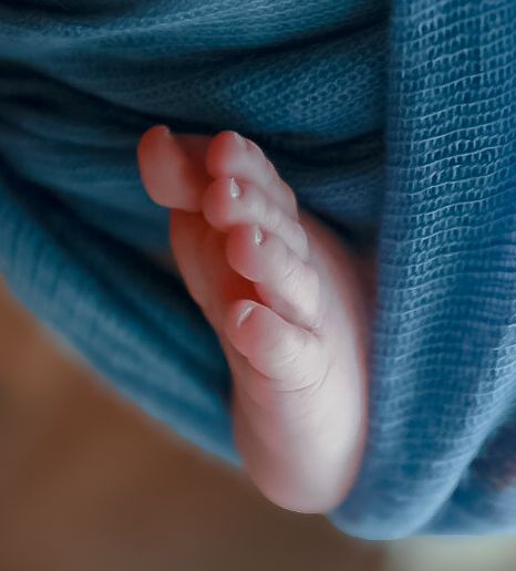 A small baby's hand gently grasps a soft blue blanket in a tender moment.