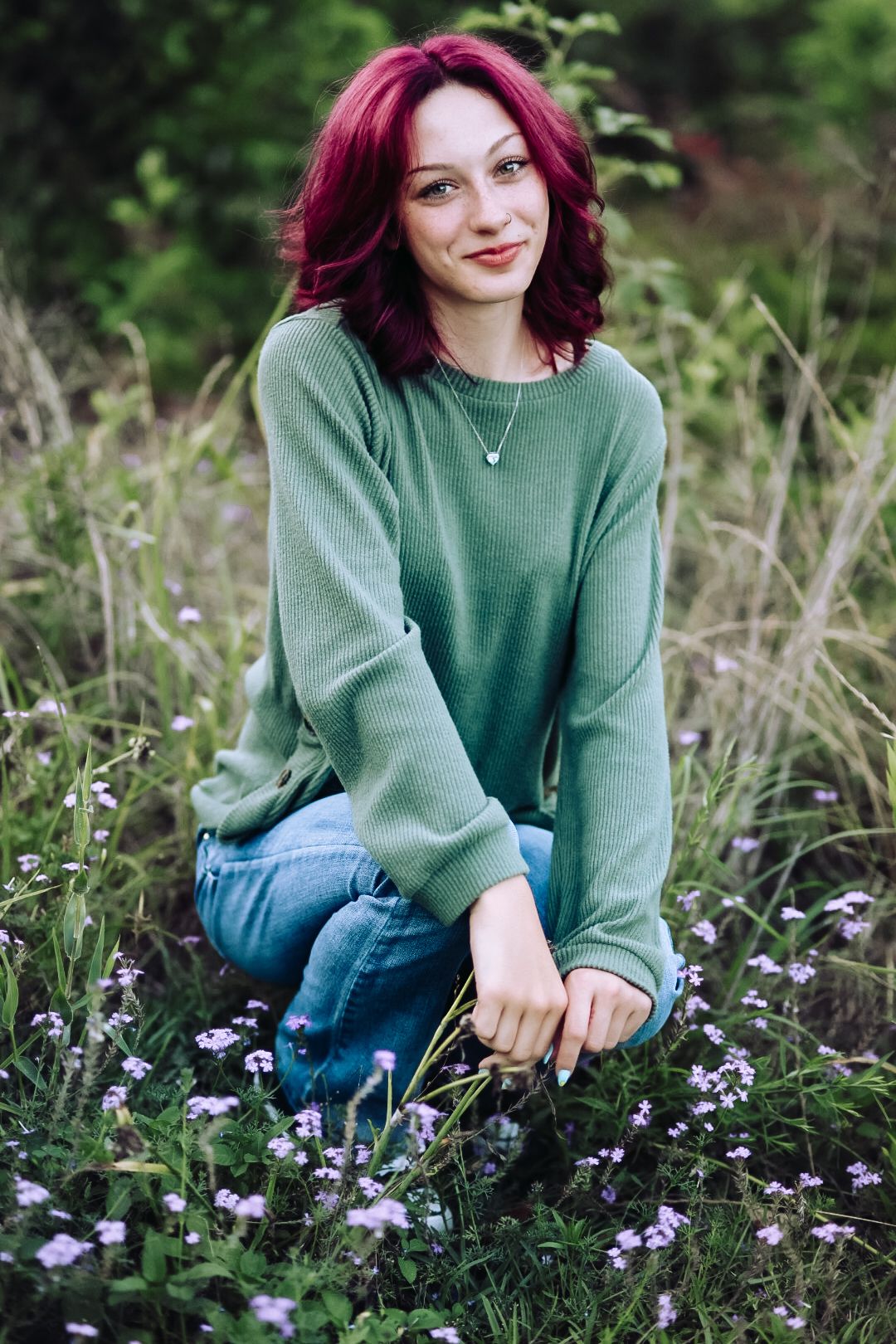 Person in green sweater sits among purple wildflowers in a natural outdoor setting.