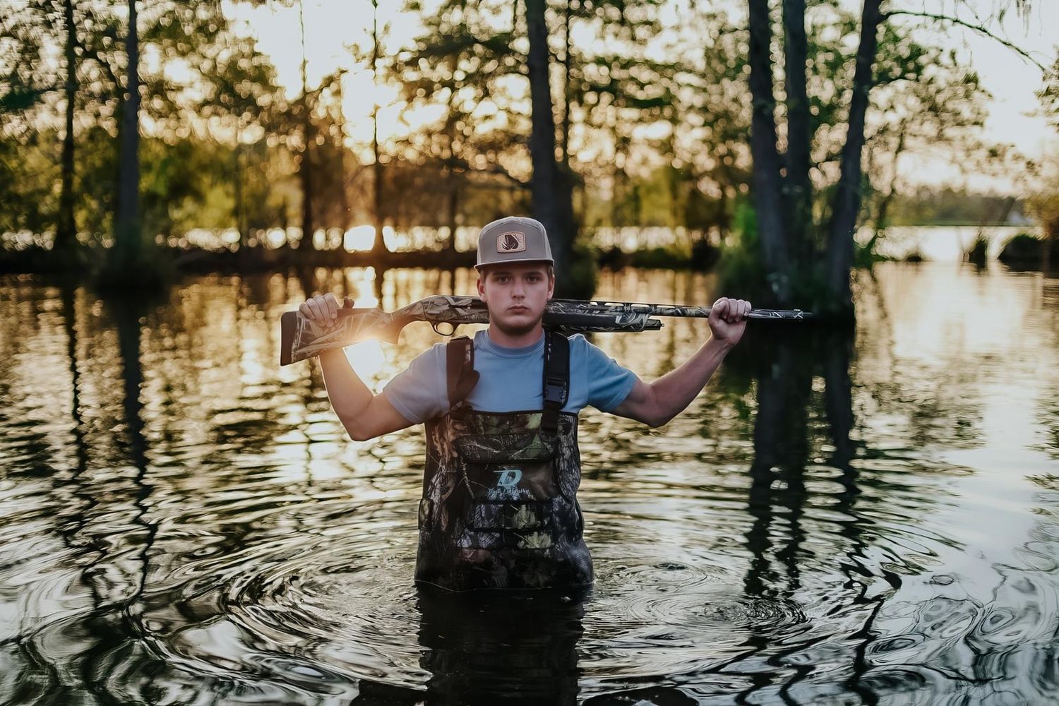 Person wading through flooded forest area with sunlight filtering through trees during golden hour.