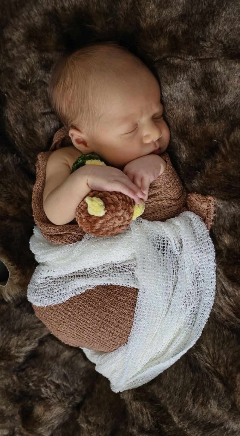 A sleeping newborn wrapped in brown and white knit blankets lies peacefully on a dark furry background.