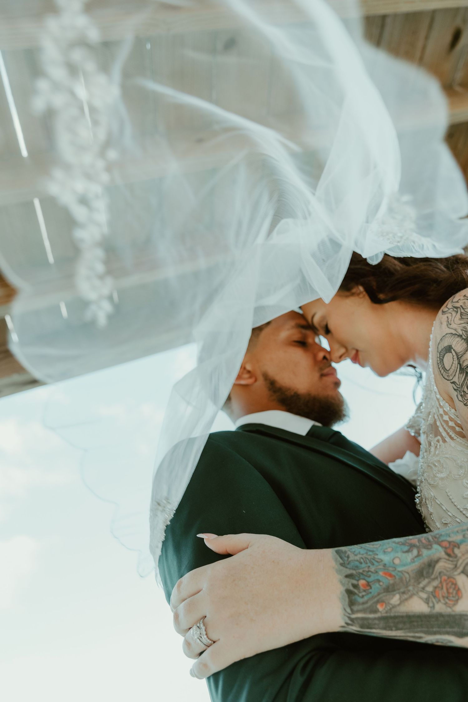 A bride and groom share an intimate forehead touch under a flowing white veil on their wedding day.
