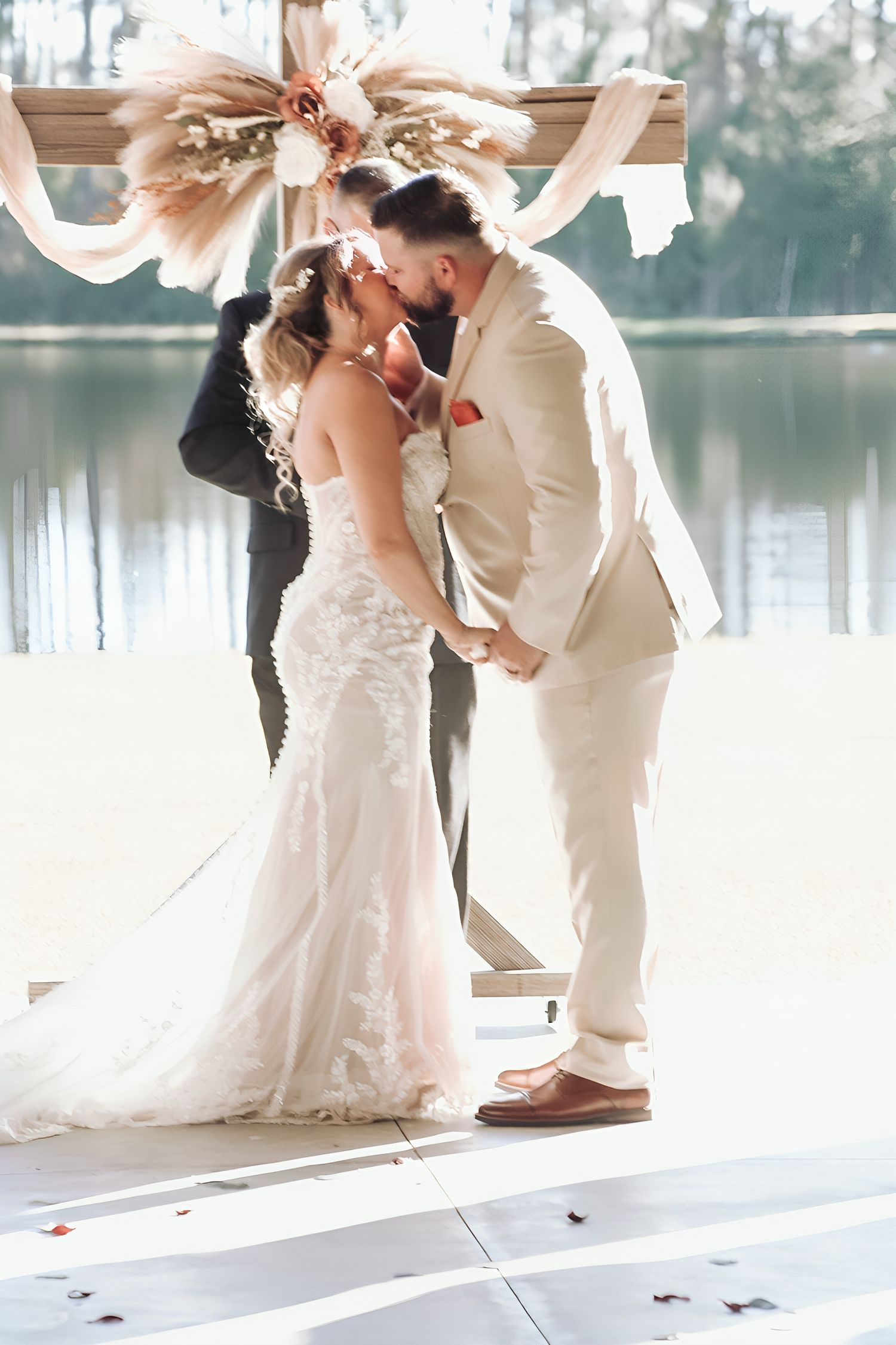 A romantic wedding couple shares a kiss in a series of elegant photos by a lakeside venue in matching white attire.