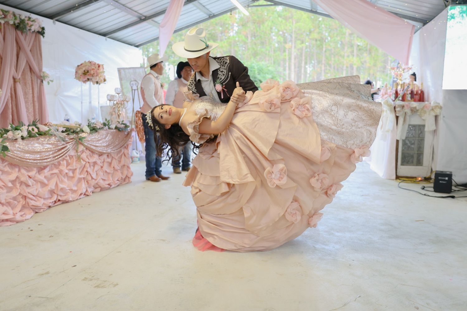 Couple dancing at a quinceanera celebration, woman in pink ballgown being dipped by partner in decorated event tent.
