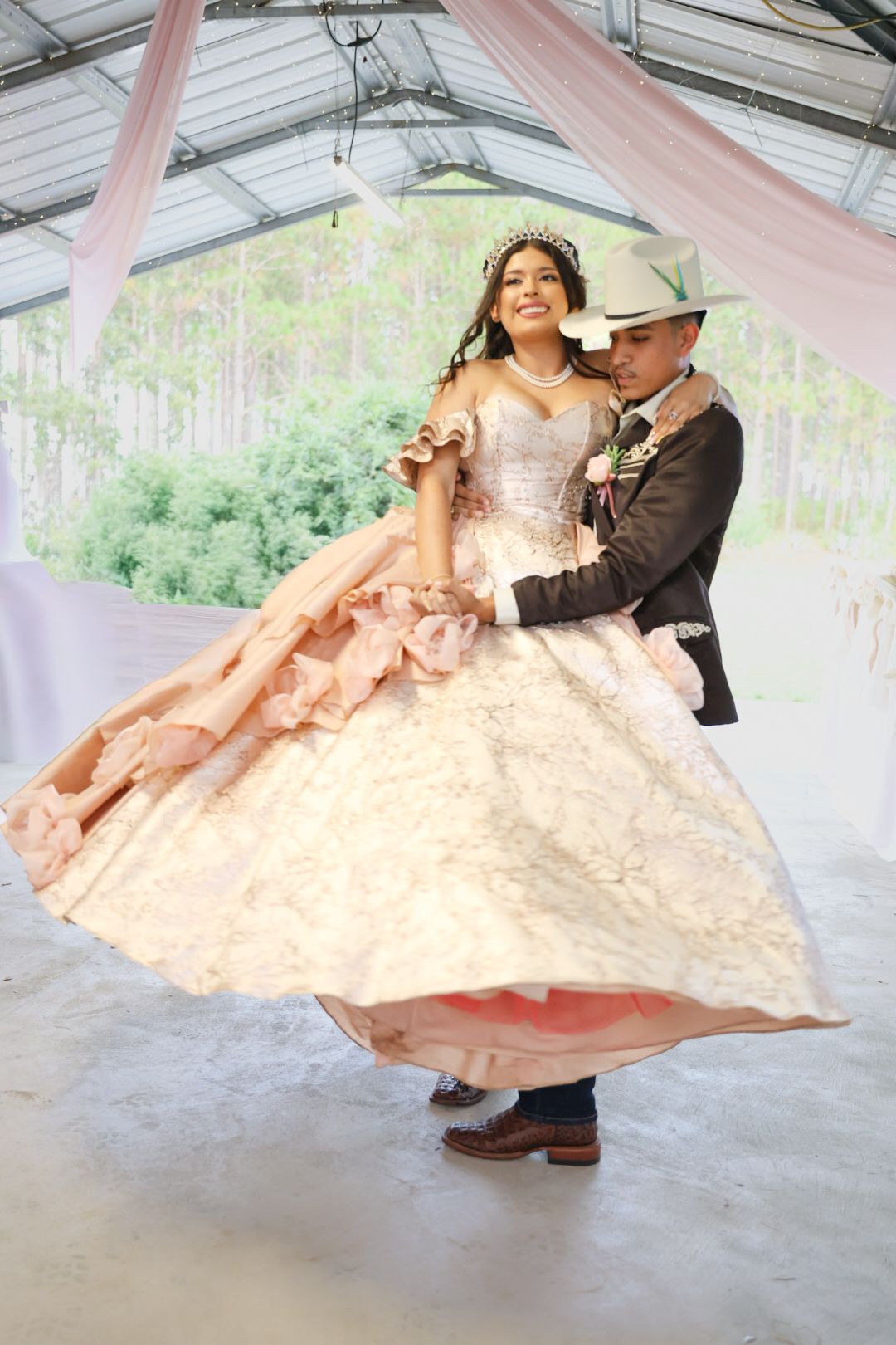 Young woman in pink quinceañera gown dances with partner in cowboy hat at elegant outdoor celebration.