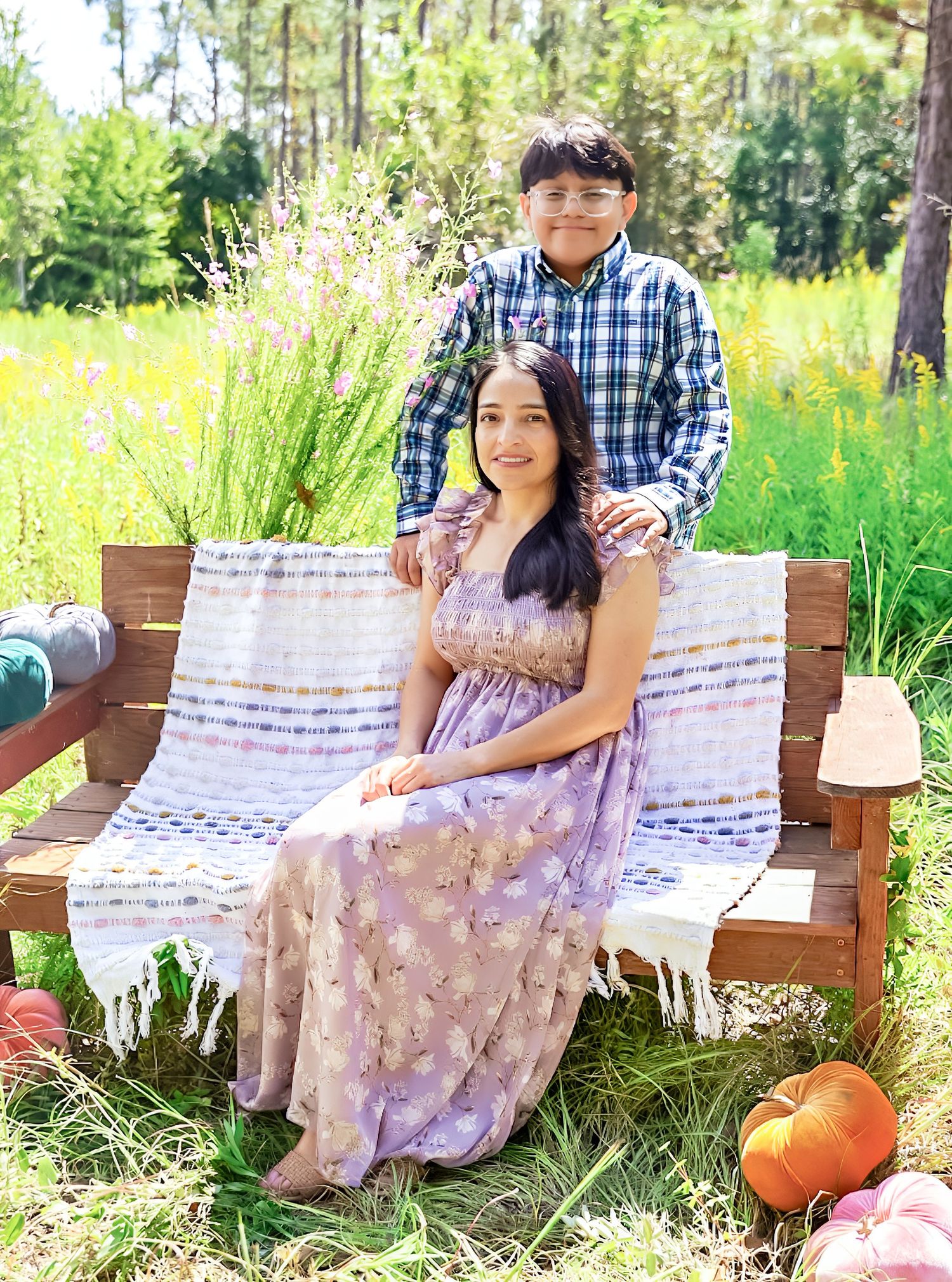 A rustic outdoor photo shoot setup with wooden benches, plaid blankets, and pumpkins in a sunlit meadow.