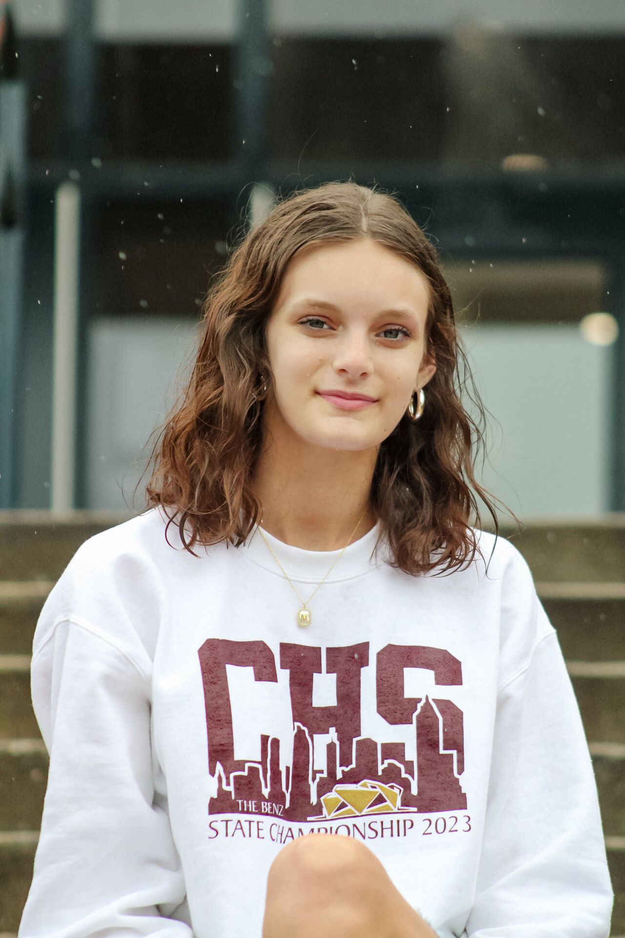 Teen girl in CHS State Championship 2023 white sweatshirt posing on school steps with wavy brown hair.