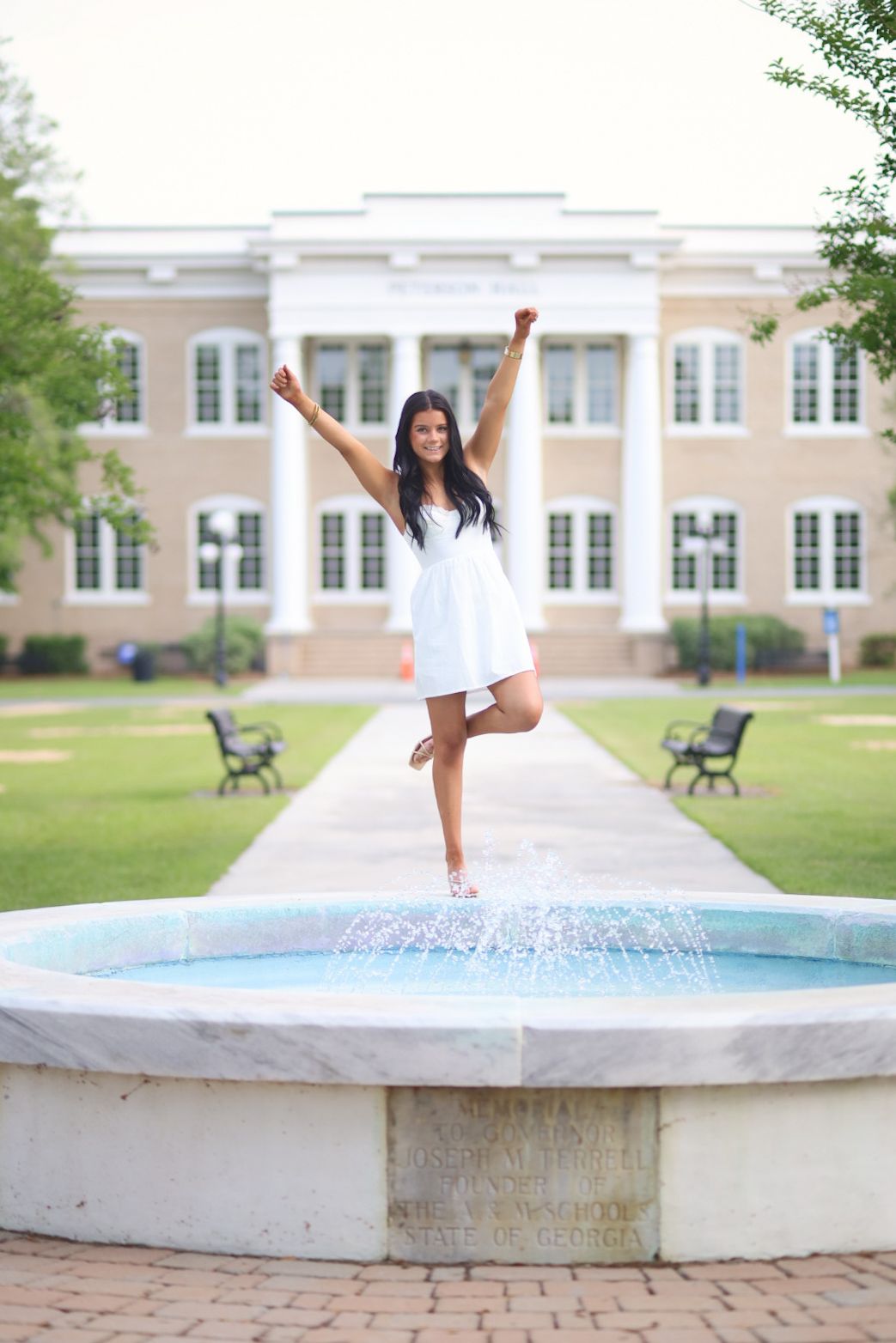 A dancer in white performs graceful ballet poses on a concrete ledge in front of a stately building.