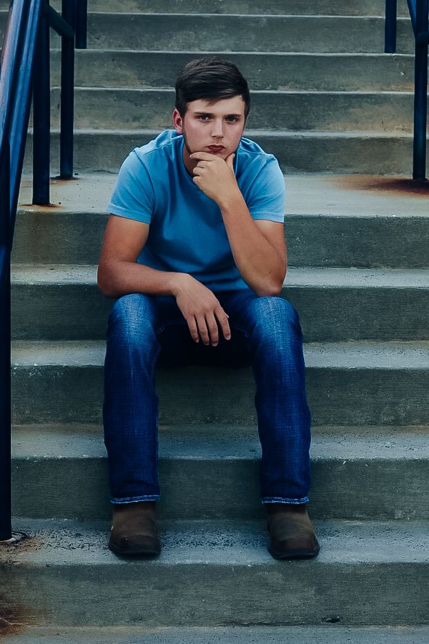 A person in blue clothing sits alone on concrete steps with a contemplative pose.