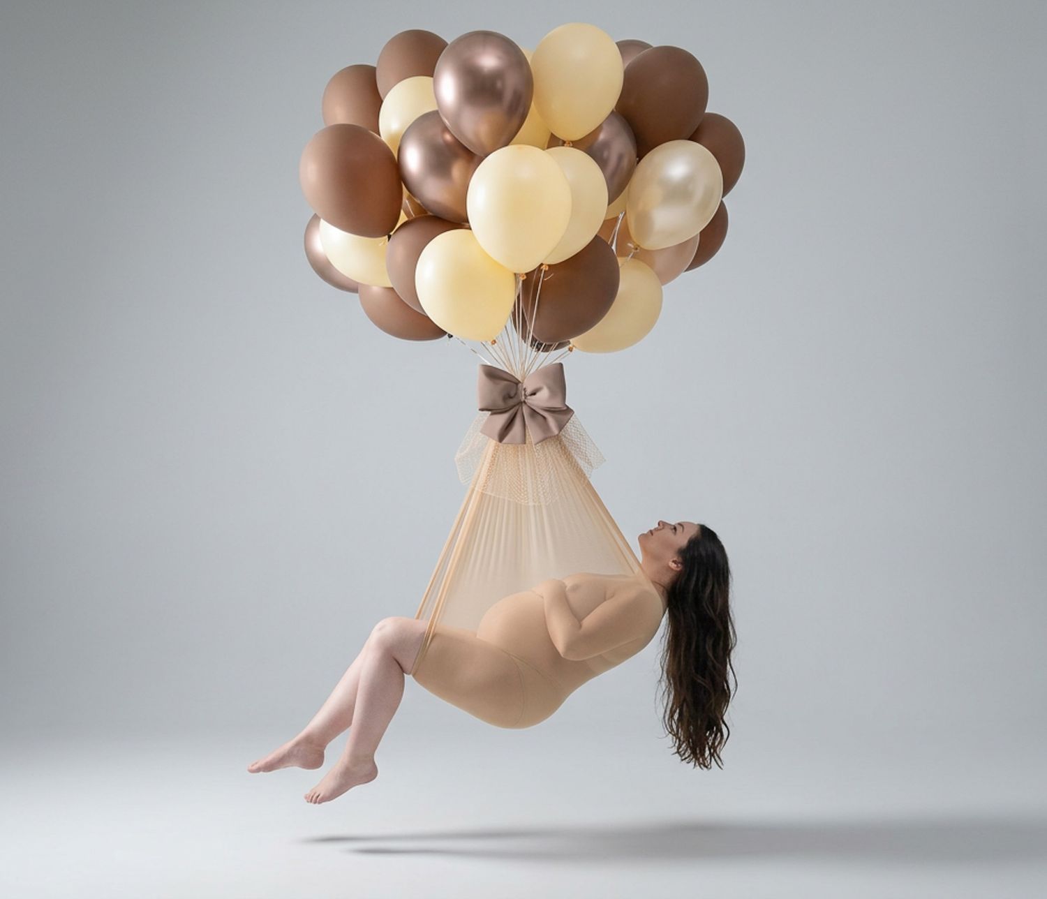 Woman suspended in air by bundle of gold, cream, and brown balloons tied with bow in artistic levitation photo.