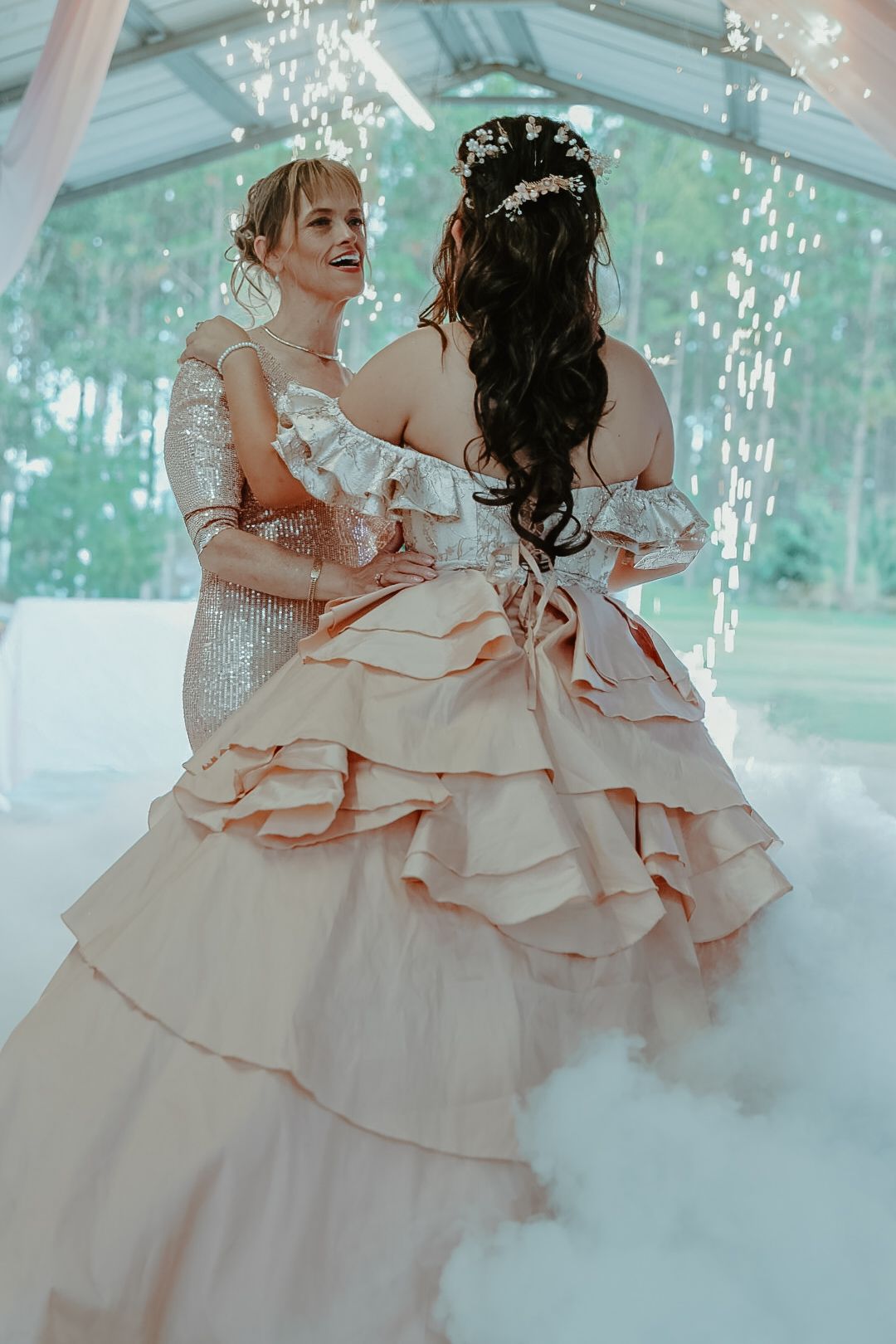 Two brides dance together in elegant gowns amid sparkling lights and fog at their wedding celebration.