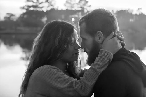 Black and white photo of a romantic couple embracing near a lake, woman tenderly holding mans face.