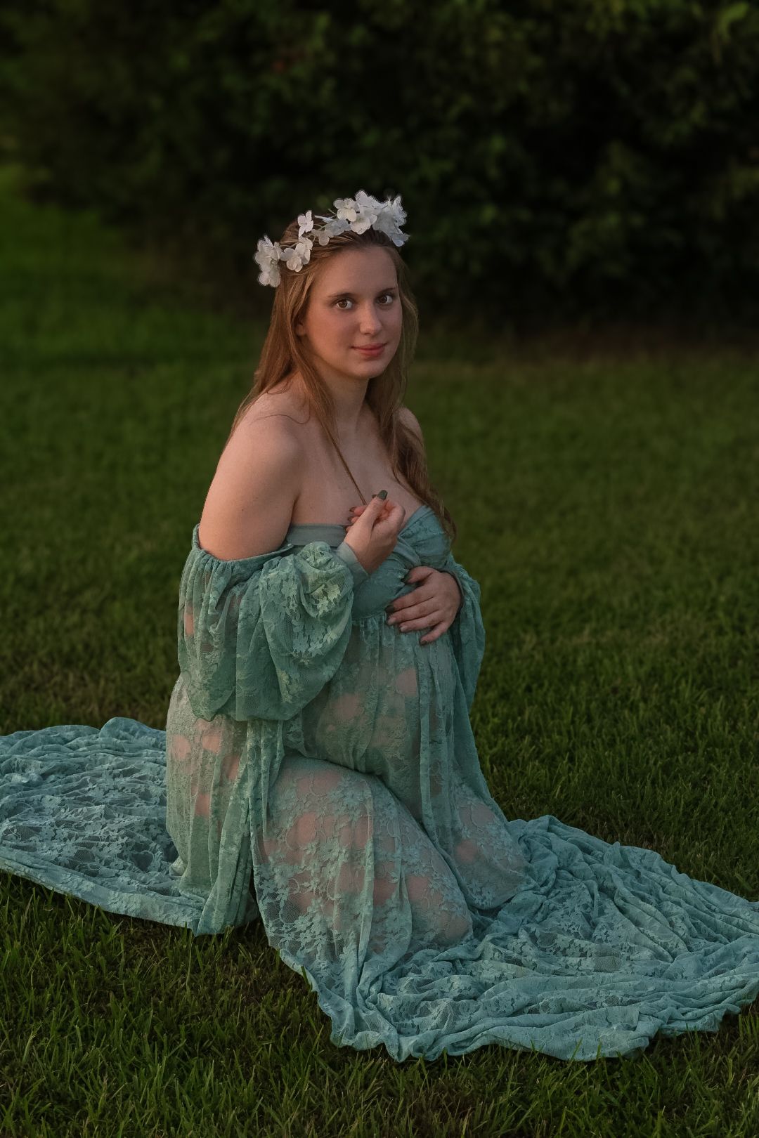 A dreamy outdoor portrait in a turquoise lace dress and floral crown sitting on grass at dusk.