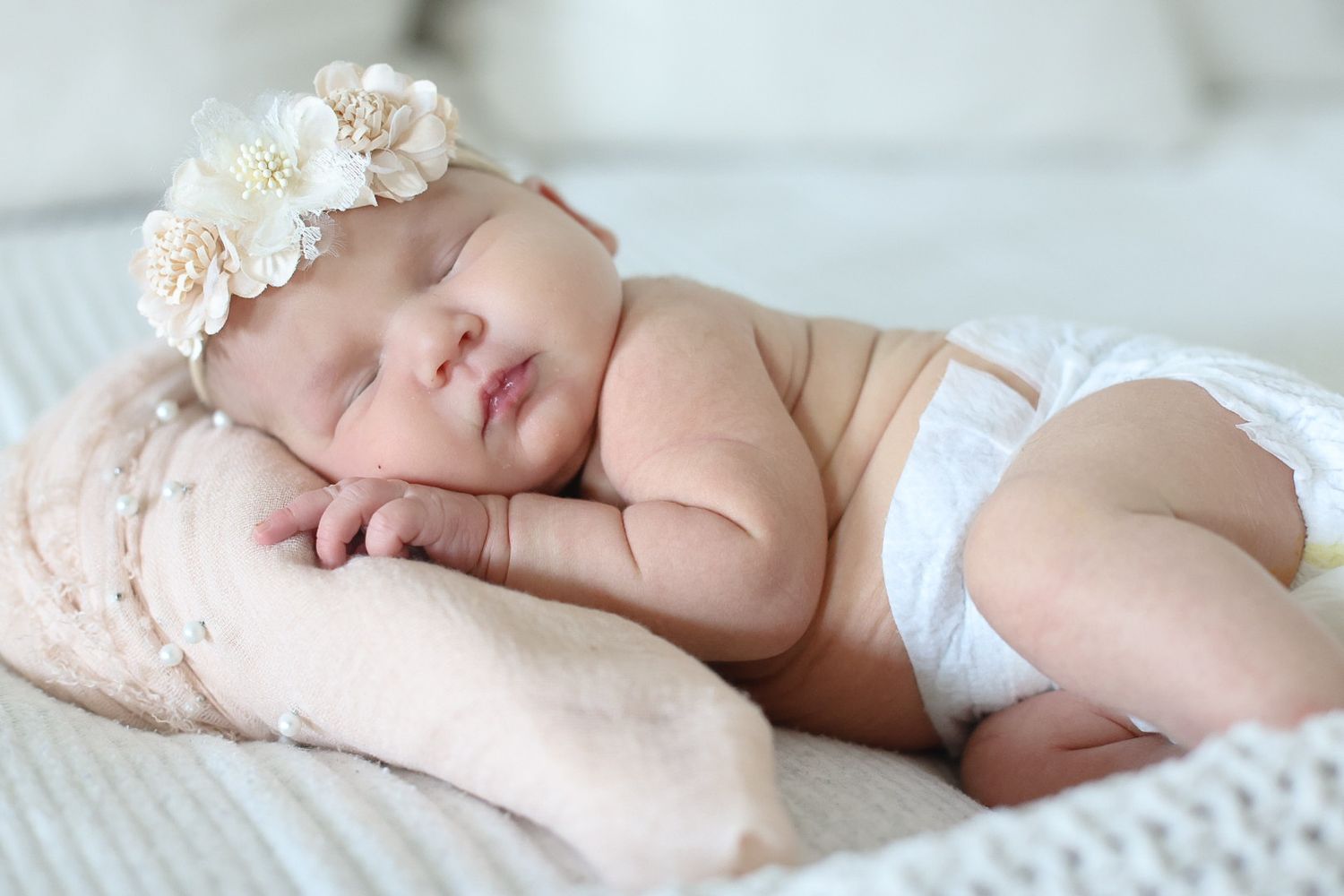 A sleeping newborn baby wrapped in white blankets lies peacefully on soft textured bedding.