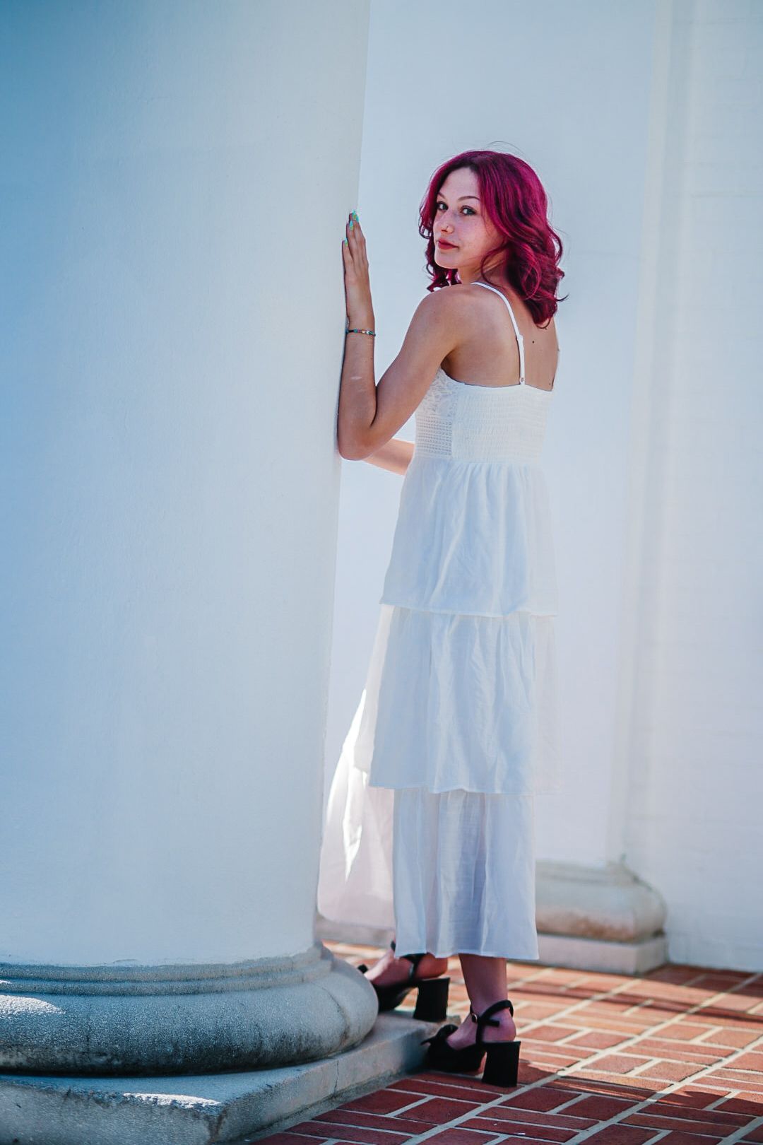 A person in a white sundress and dark shoes poses against a white wall in a series of artistic shots.