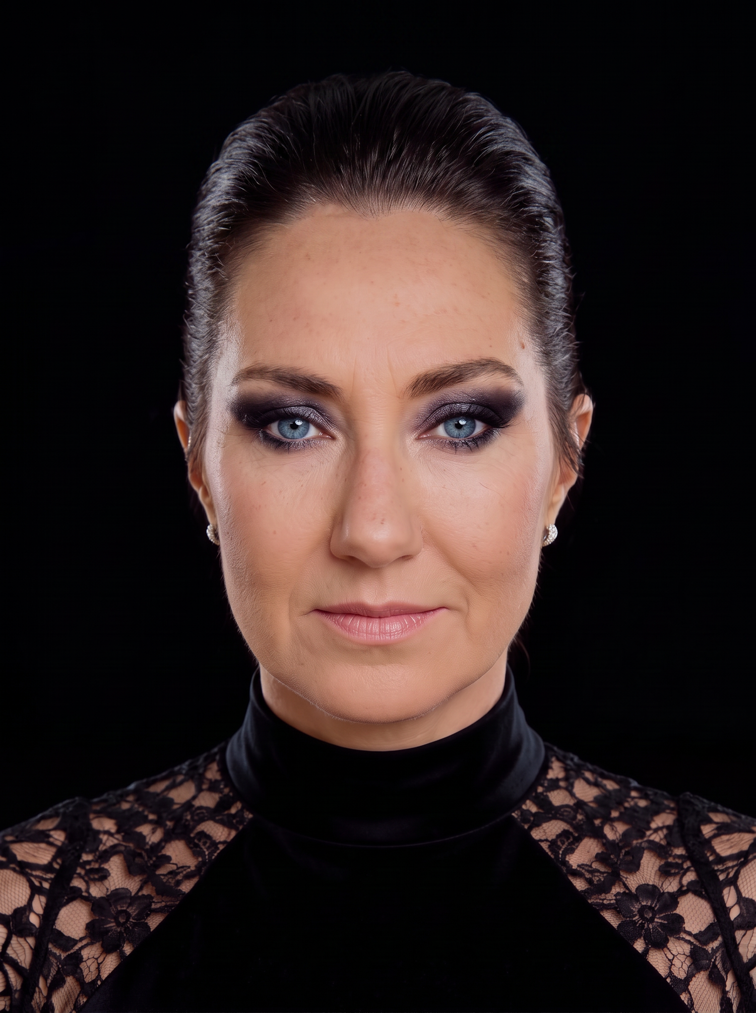 Woman with blue eyes, smoky eye makeup, slicked-back dark hair, wearing a black lace turtleneck top.