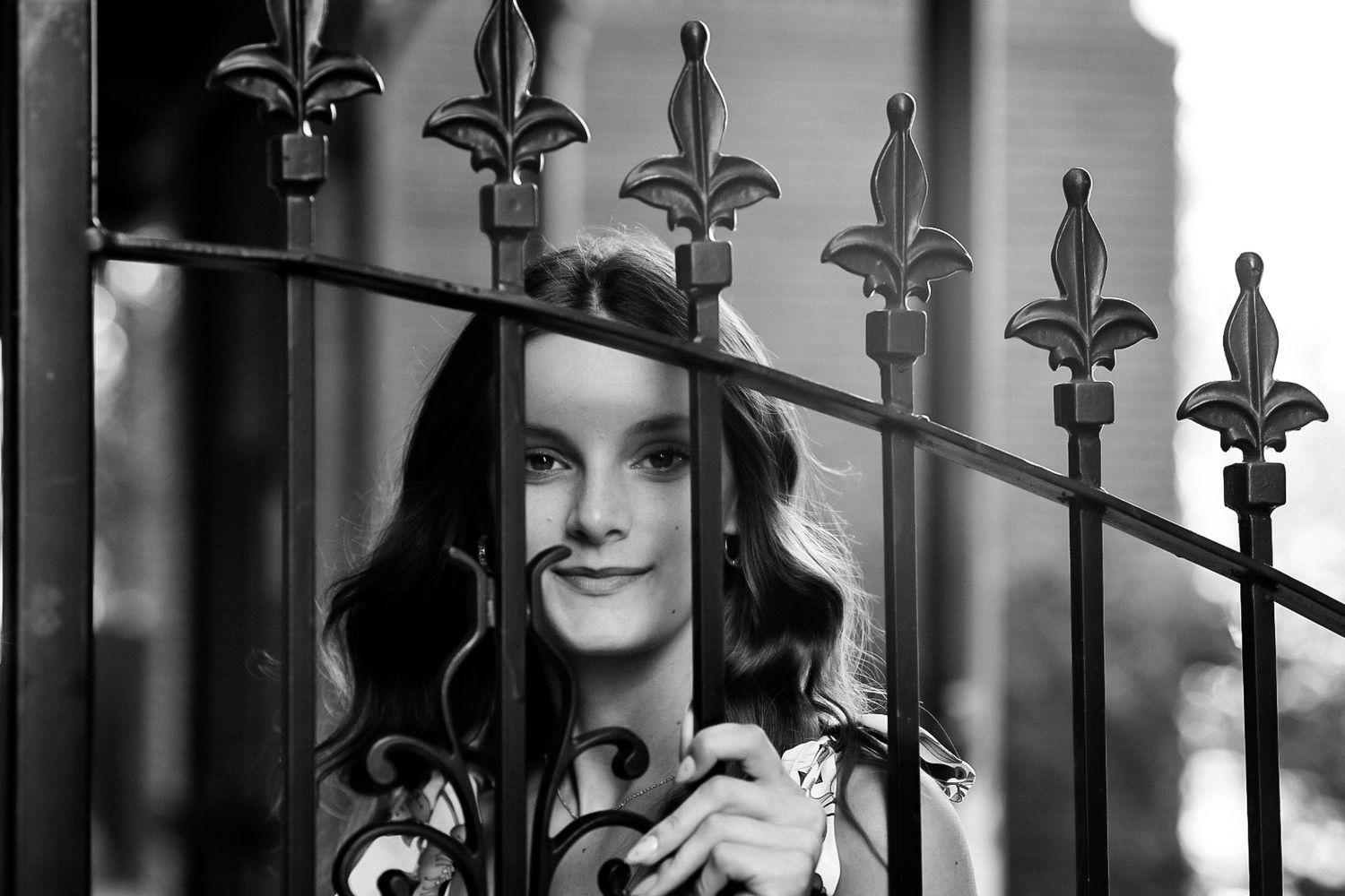Young woman smiling through ornate black iron gate in black and white photo.
