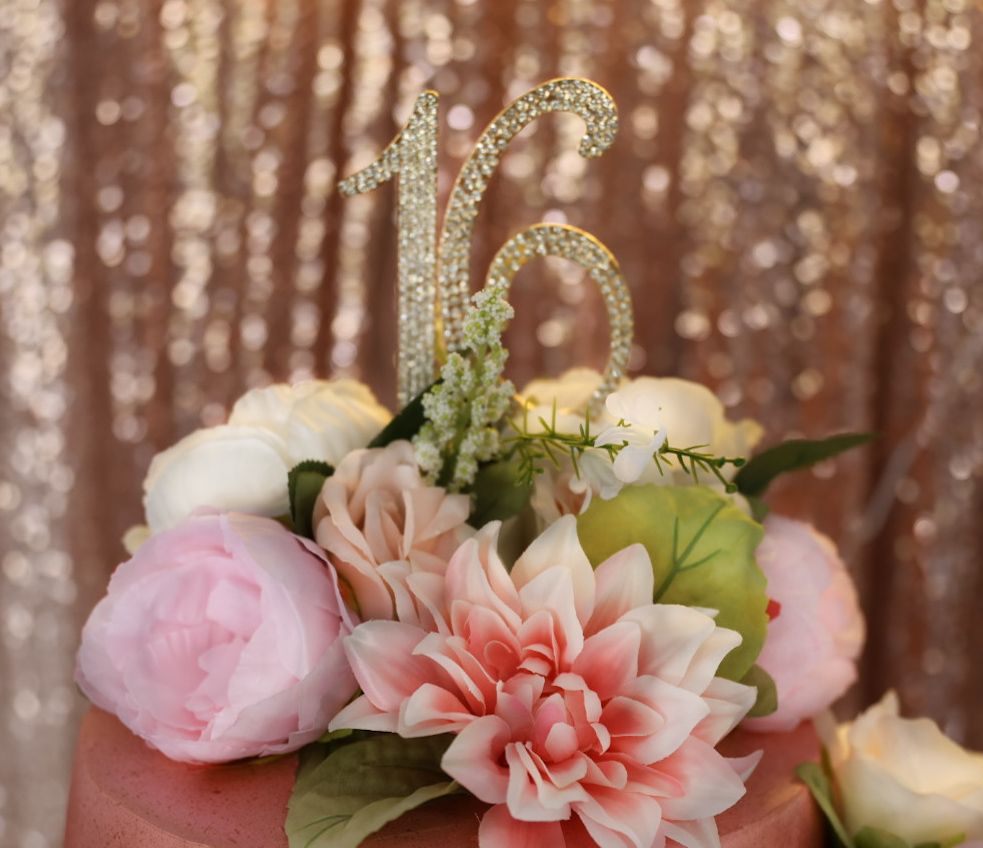 Sweet 16 birthday cake topper with rhinestone numbers on floral cake with pink peonies and roses.