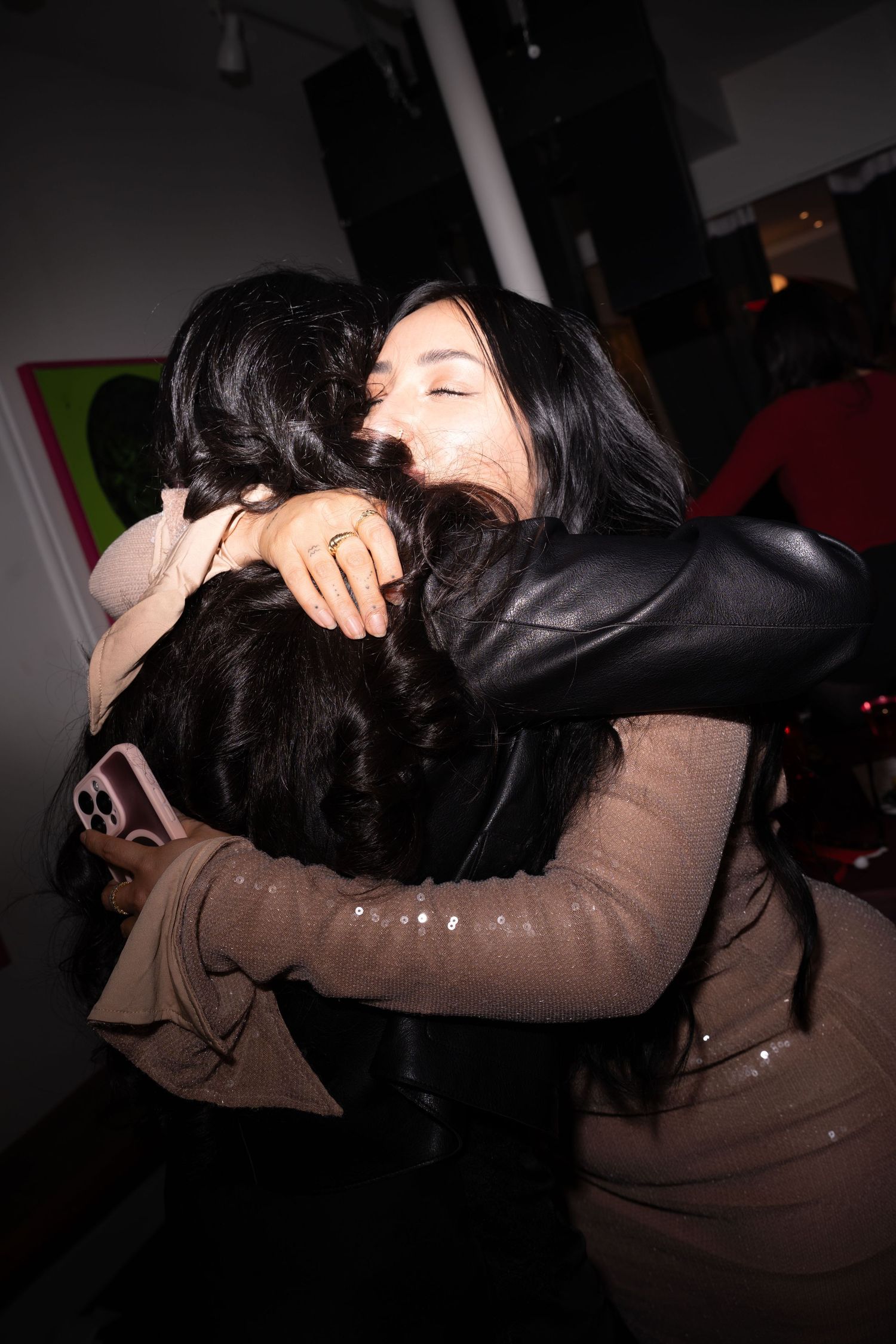Two women share a warm embrace at an indoor art gallery social event.