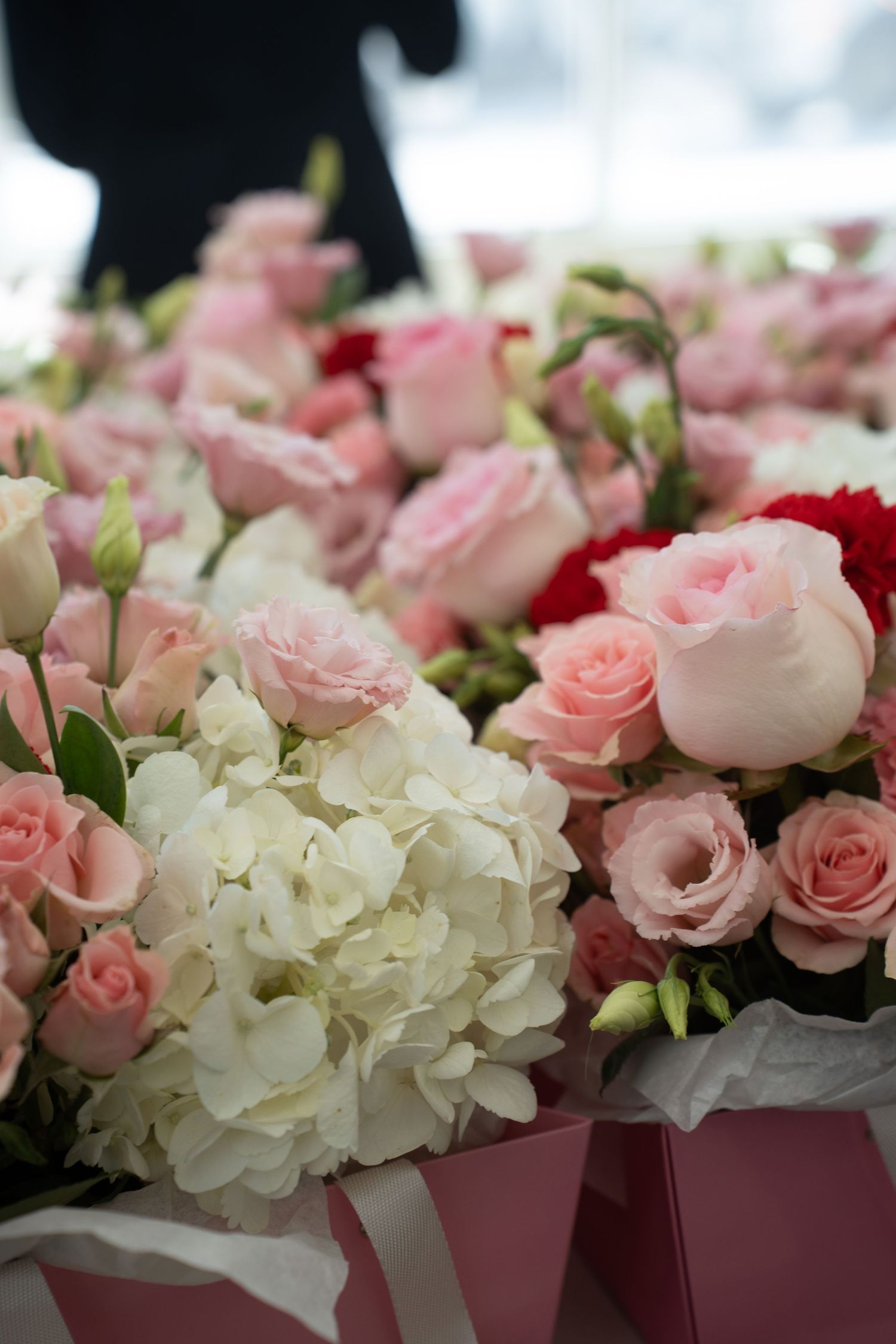 Elegant arrangement of pink roses and white hydrangeas in pink gift boxes at an event.