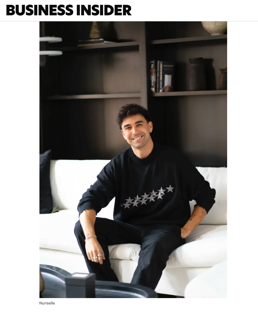 Business Insider feature of man in black star sweatshirt sitting on white sofa smiling.