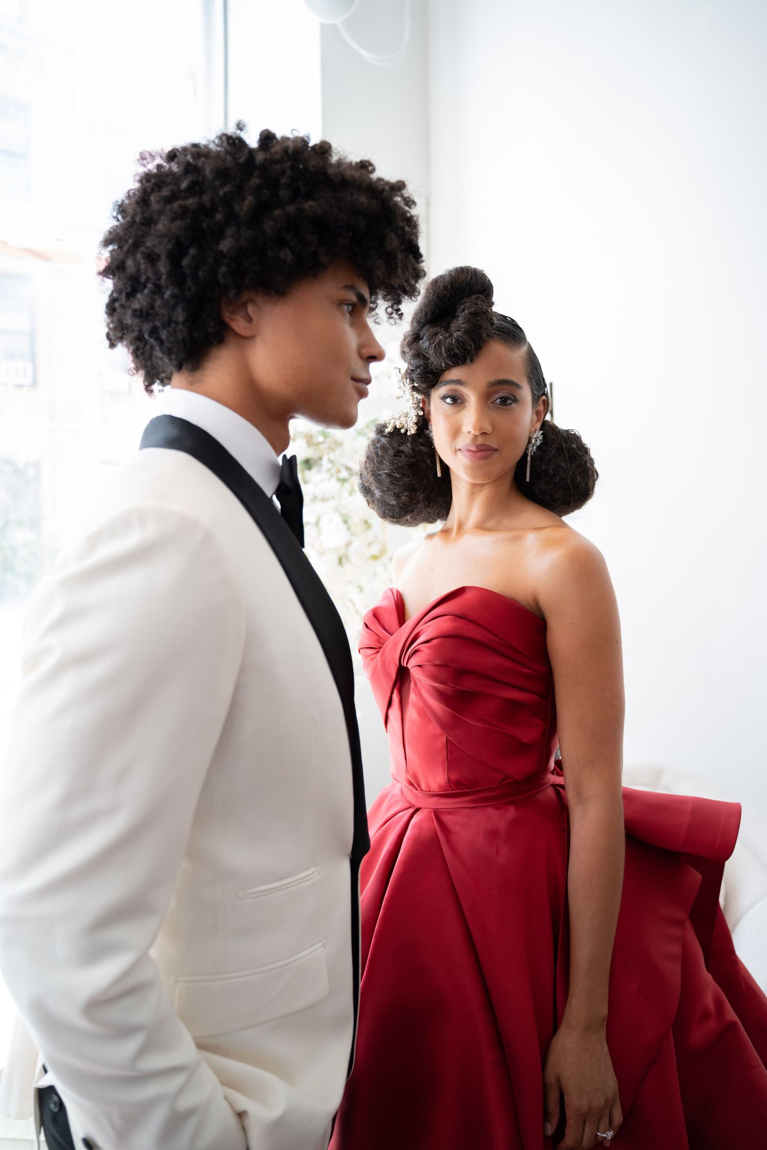 Young Black couple in elegant wedding attire, groom in white tuxedo, bride in strapless red ball gown.
