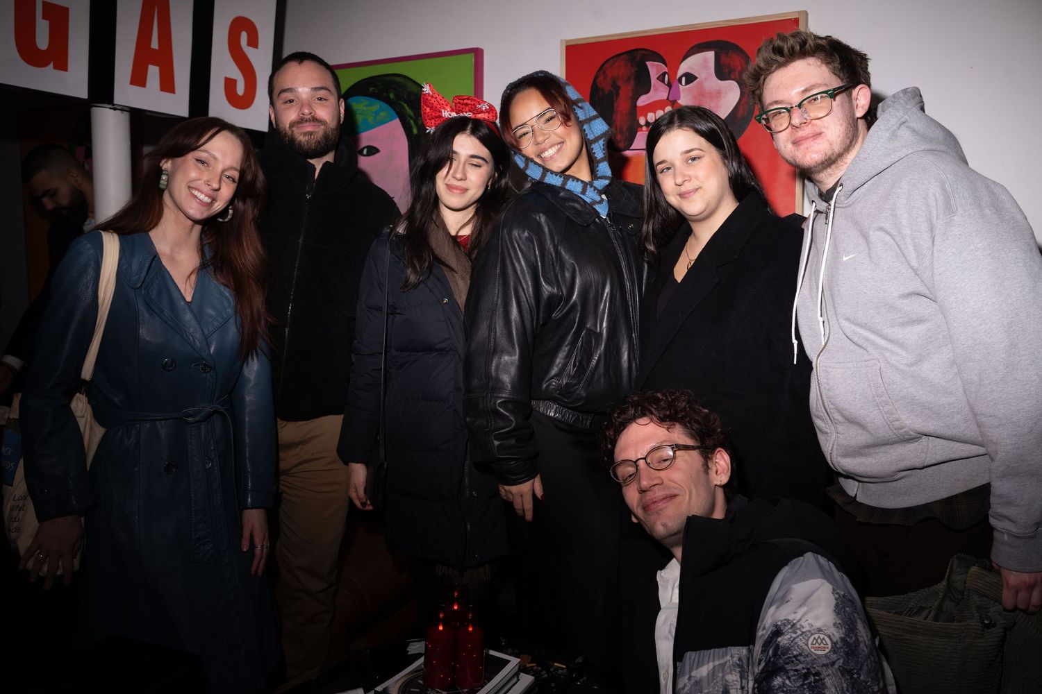 Group of seven friends posing together at an art gallery event with colorful paintings on the wall.
