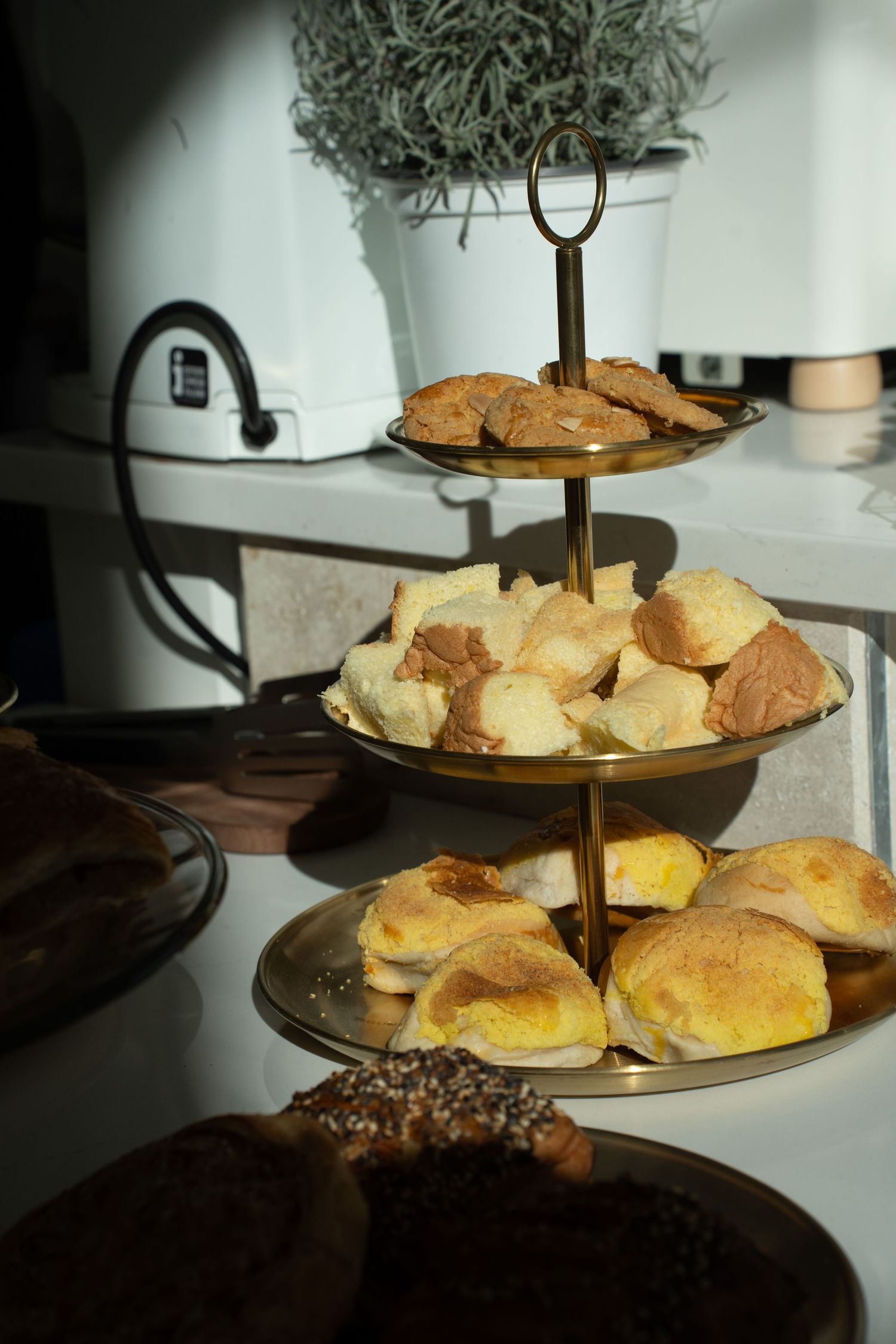Gold three-tiered serving stand filled with assorted pastries and bread rolls at a catered event.