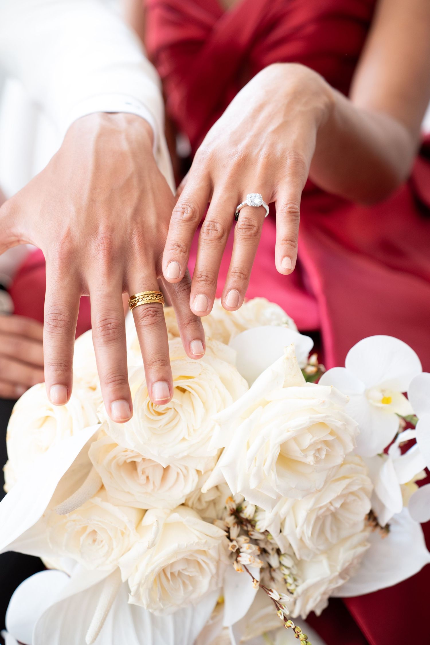 Close-up of newlyweds hands with gold wedding rings over white rose bridal bouquet.