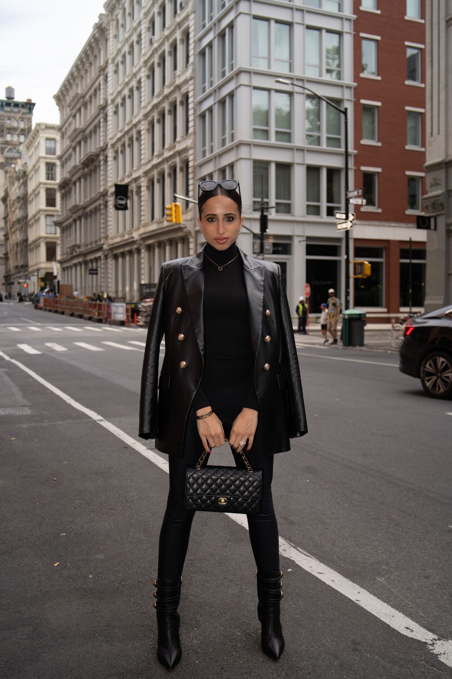 Fashion blogger in all-black leather blazer outfit holding quilted Chanel bag on a New York City street.
