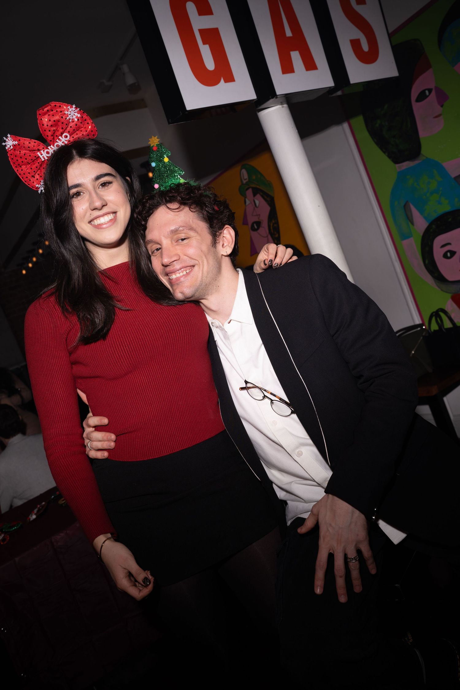 Couple smiling together at a festive holiday party with Christmas decorations in background.